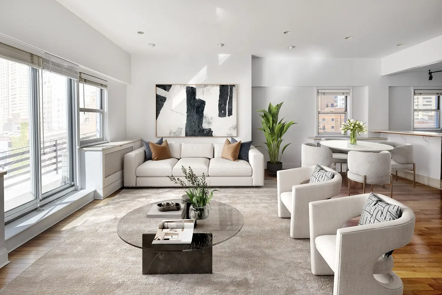 Modern living room from a real estate property listed by Adam Gerber, with white walls, large windows, a white sofa with throw pillows, armchairs, a glass coffee table, a green potted plant, and abstract artwork on the wall.
