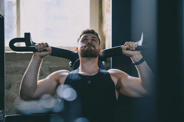 A man lifting a barbell behind his neck during a workout in a gym.