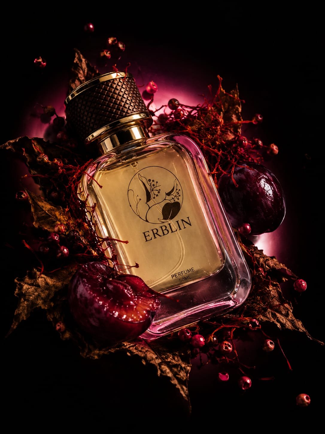 A glass perfume bottle labeled 'ERBLIN' surrounded by dried leaves, red berries, and a halved cherry, with a dark background and pink lighting emphasizing the arrangement