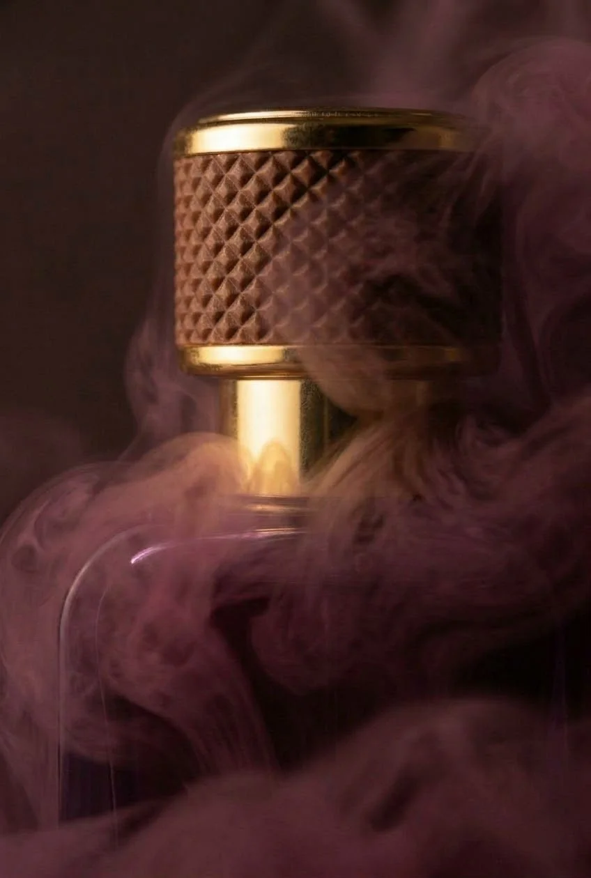 A close-up photograph of a vintage-style microphone with a textured brown grille surrounded by swirling purple smoke.