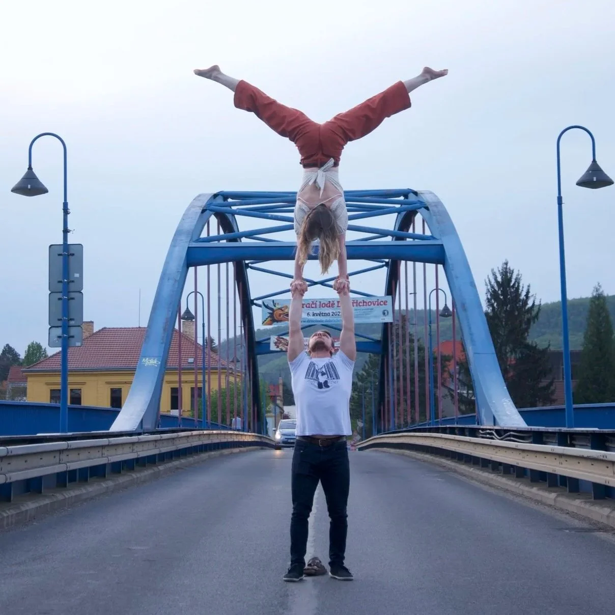 Two acrobats perform a human balancing act of a hand-to-hand on a blue bridge, one standing and holding the other upside down by the hands.