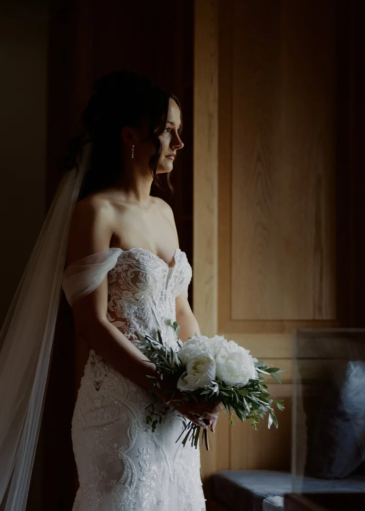 Bride holding a bouquet by a window