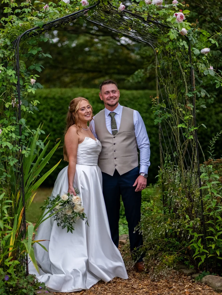 Bride and groom smiling under a garden arch