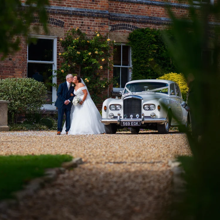 Bride and groom kissing beside a vintage wedding car