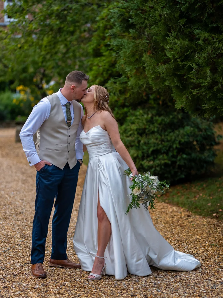 Groom kissing bride’s cheek on a gravel path