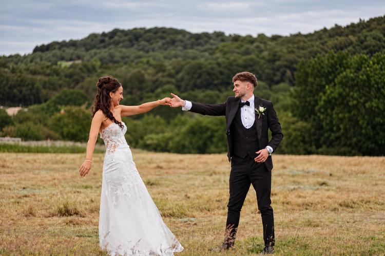 Bride and groom reaching for each other in a hayfield
