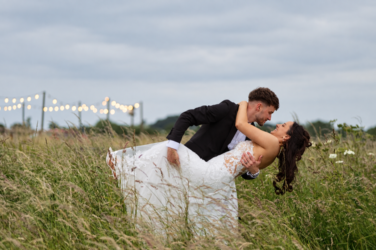Groom dipping bride for a kiss in tall grass