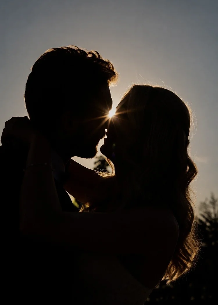 Silhouette of bride and groom kissing at sunset