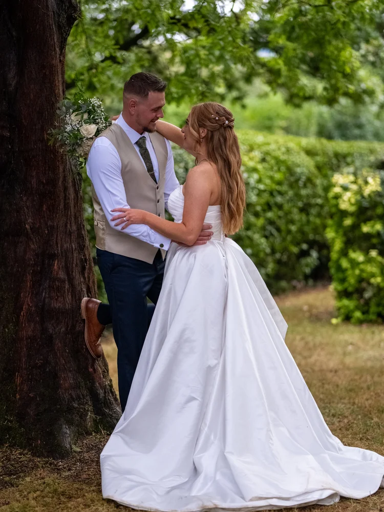 Bride and groom embracing beneath a large tree