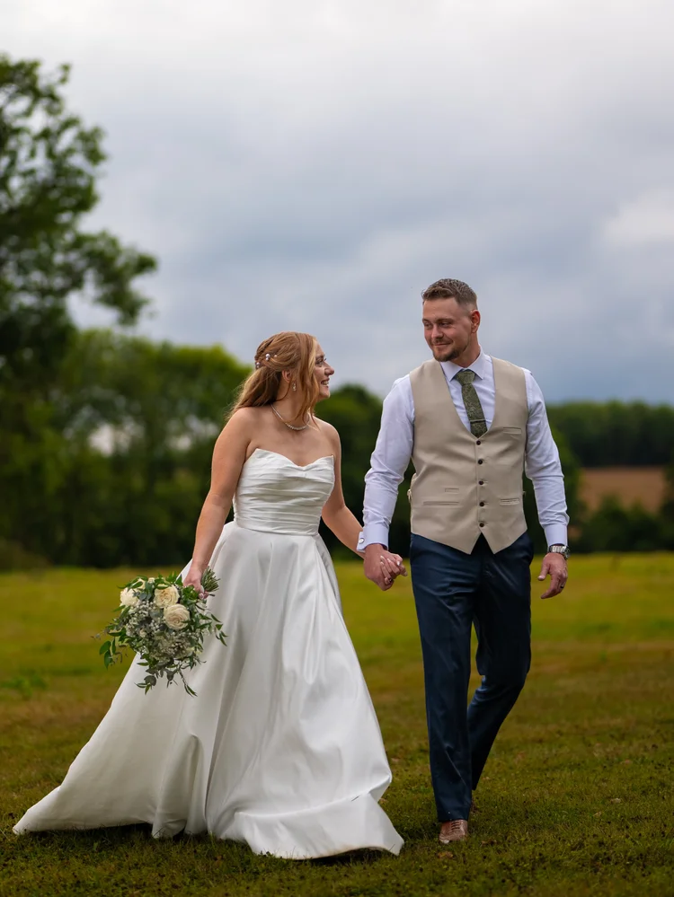 Bride and groom walking hand in hand across a lawn