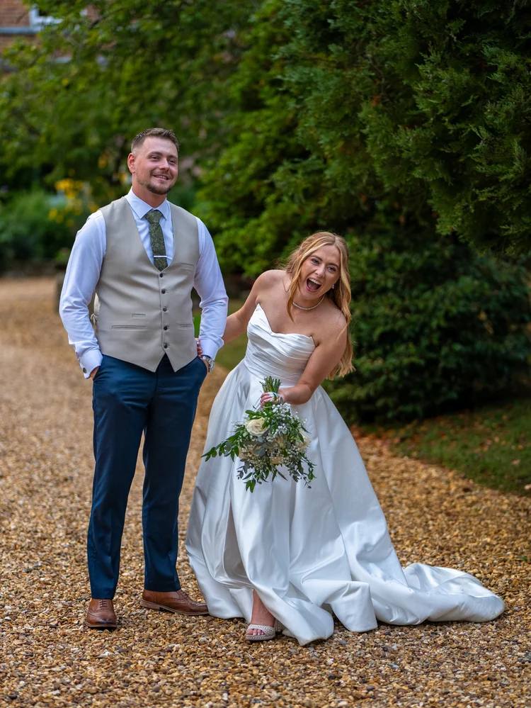 Bride lifting her gown as groom smiles on a gravel path