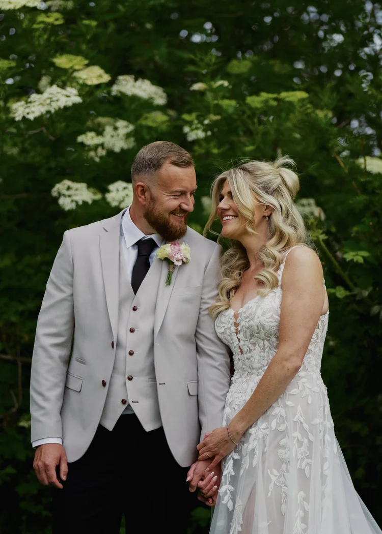 Bride laughing beside the groom by flowering shrubs