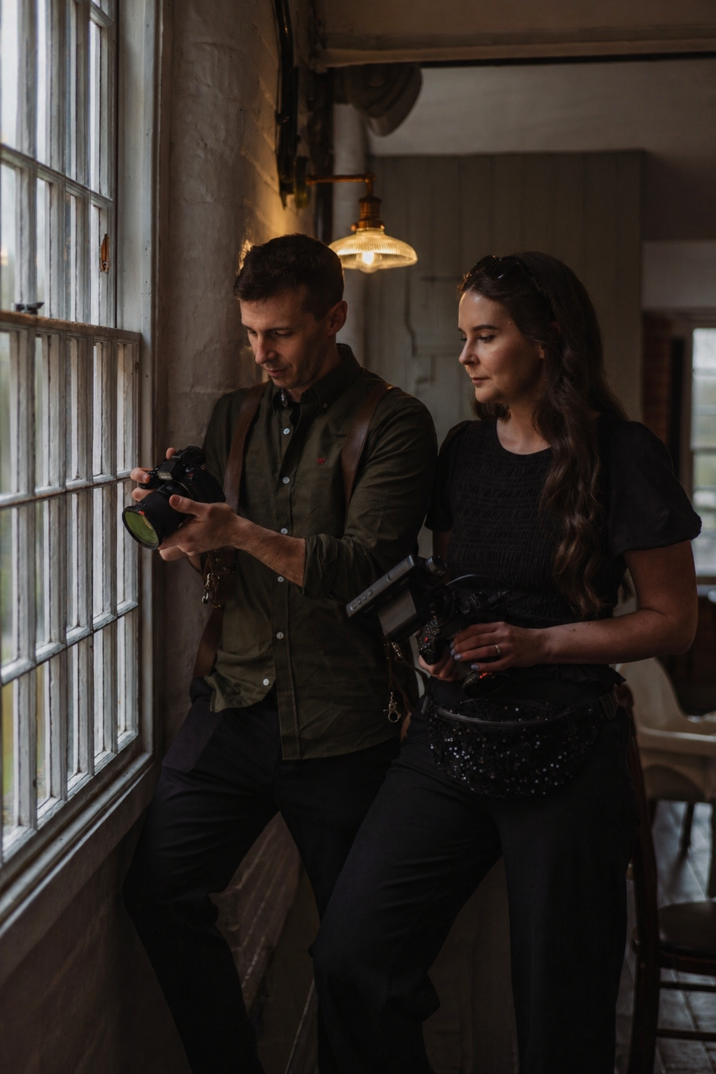 Aaron and Becky, wedding videographers, checking footage on their cameras by a window