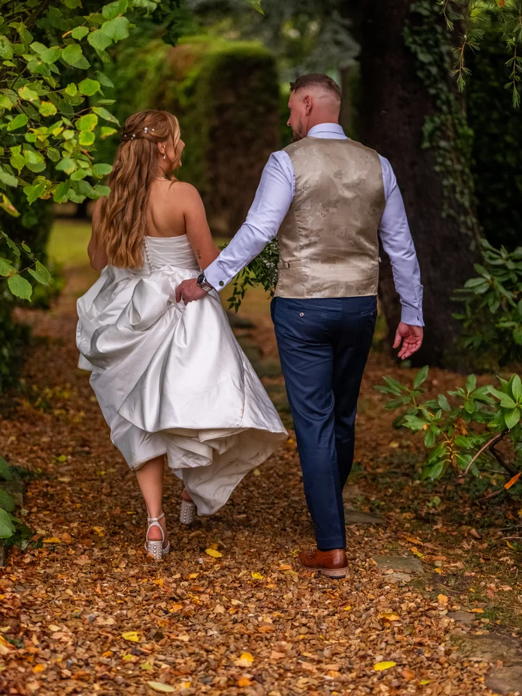 Bride and groom walking away along a leaf-covered path