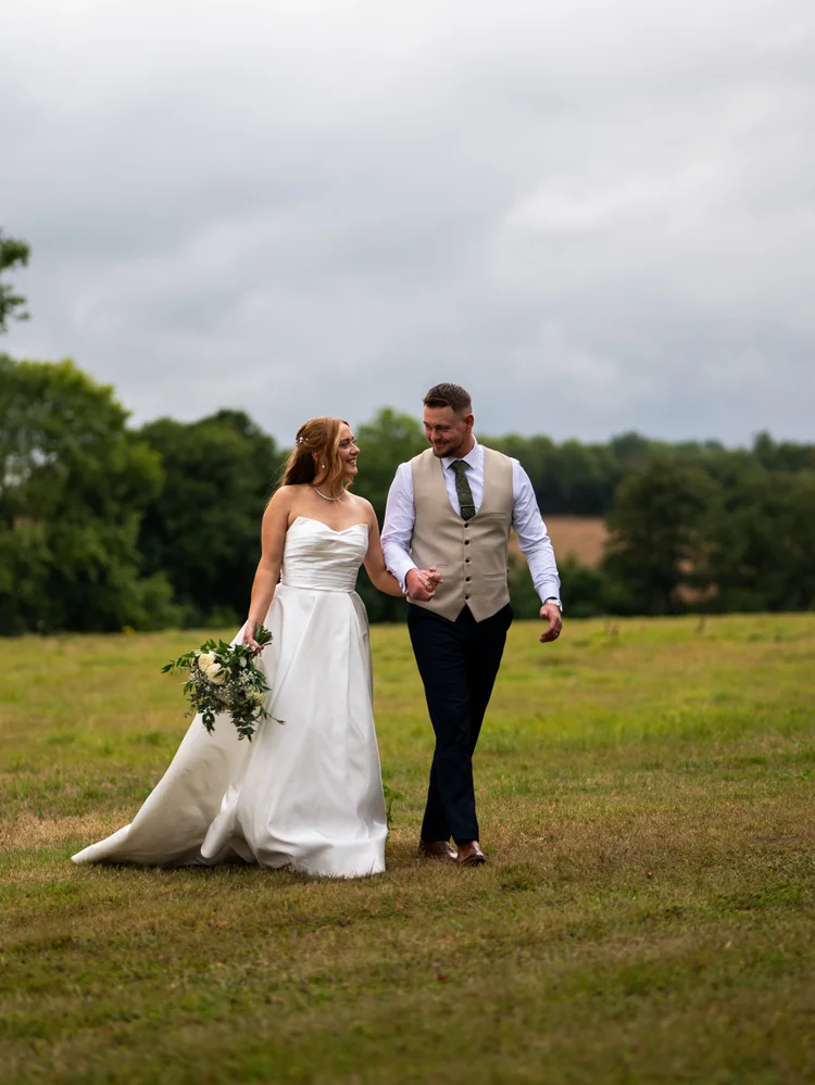 Bride and groom walking in a field under a cloudy sky