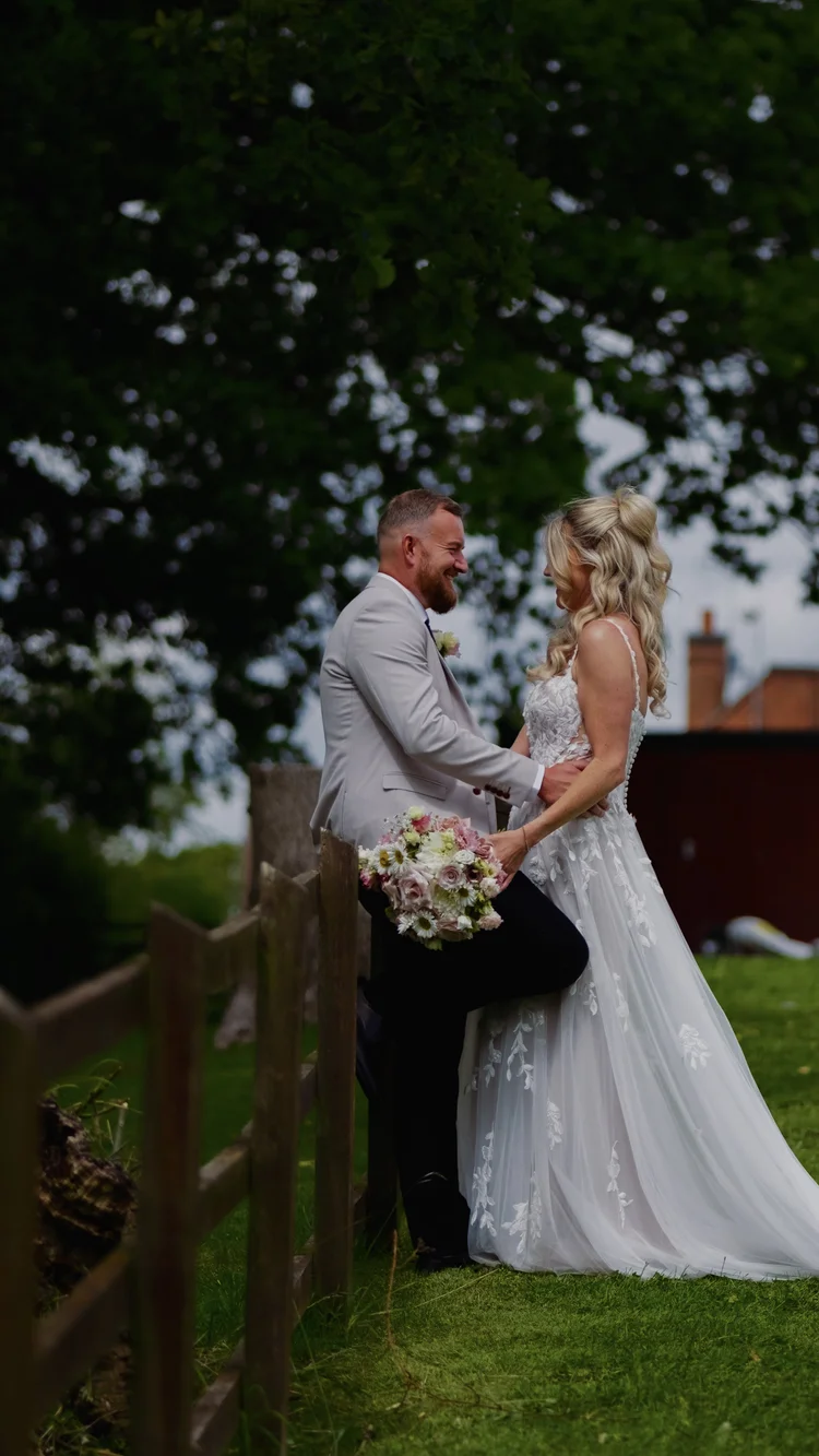 Bride and groom holding each other beside a wooden fence