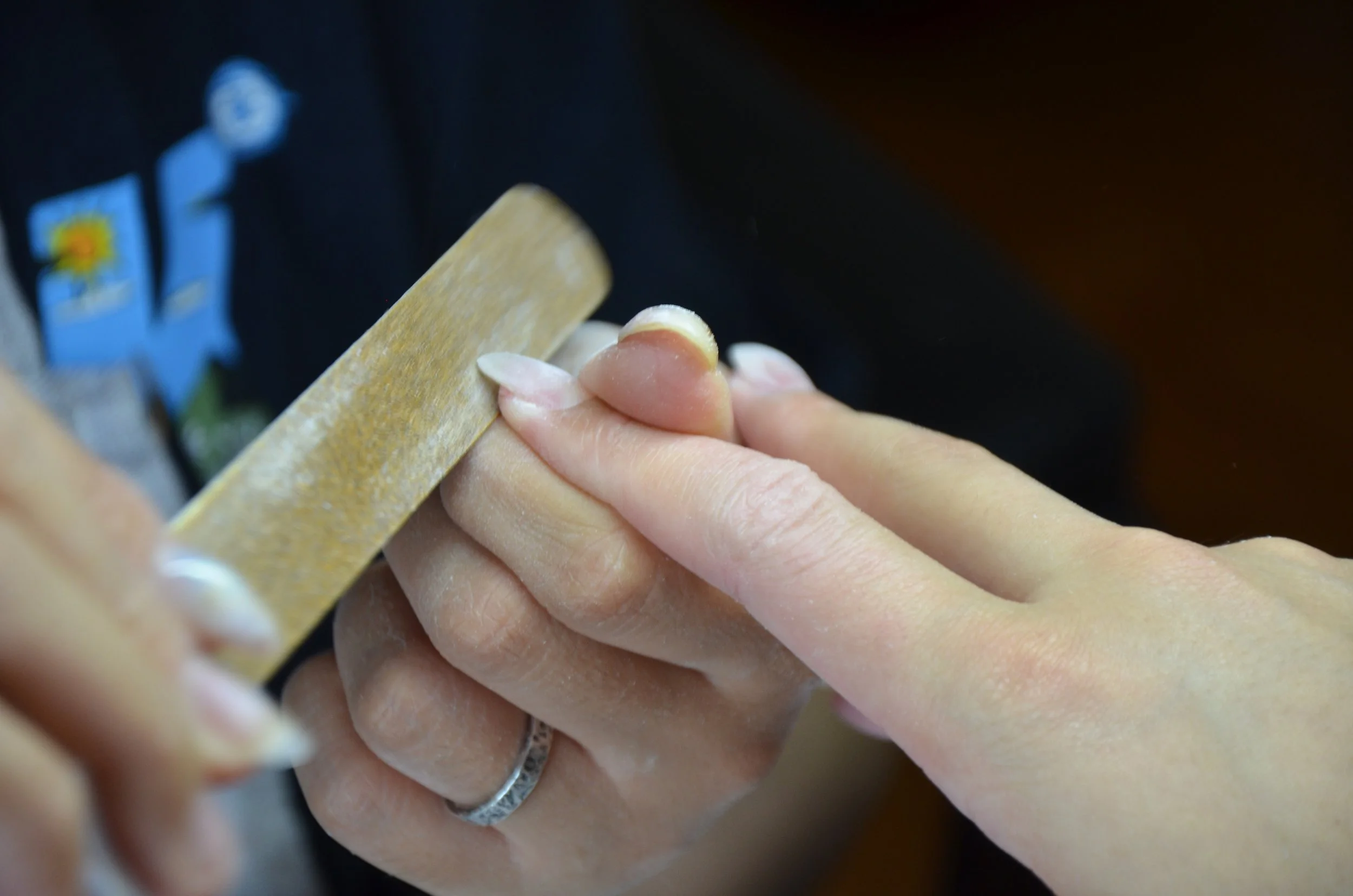 Close-up view of a person's hand with polished nails filing the nails of another person's hand with a yellow nail file.
