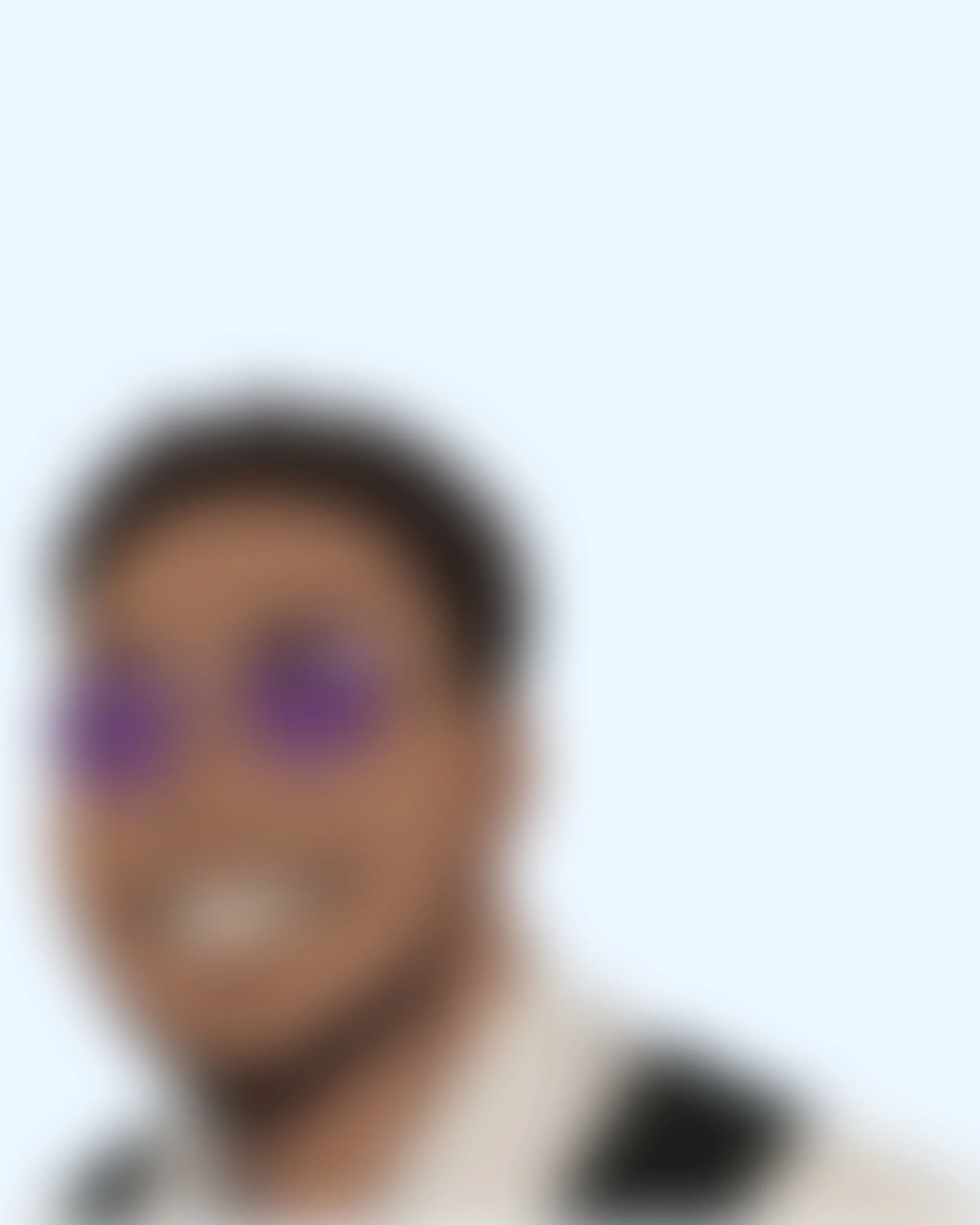 Blurry image of a person wearing purple-tinted glasses and smiling.