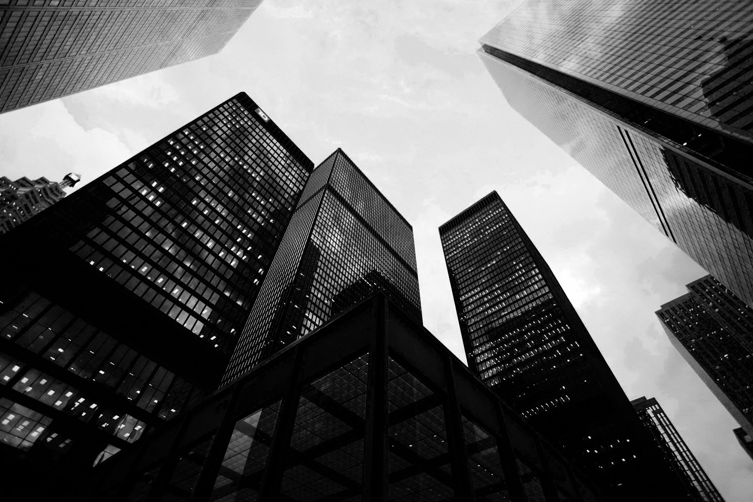 Black and white photo of tall skyscrapers with glass windows, viewed from below against a cloudy sky.
