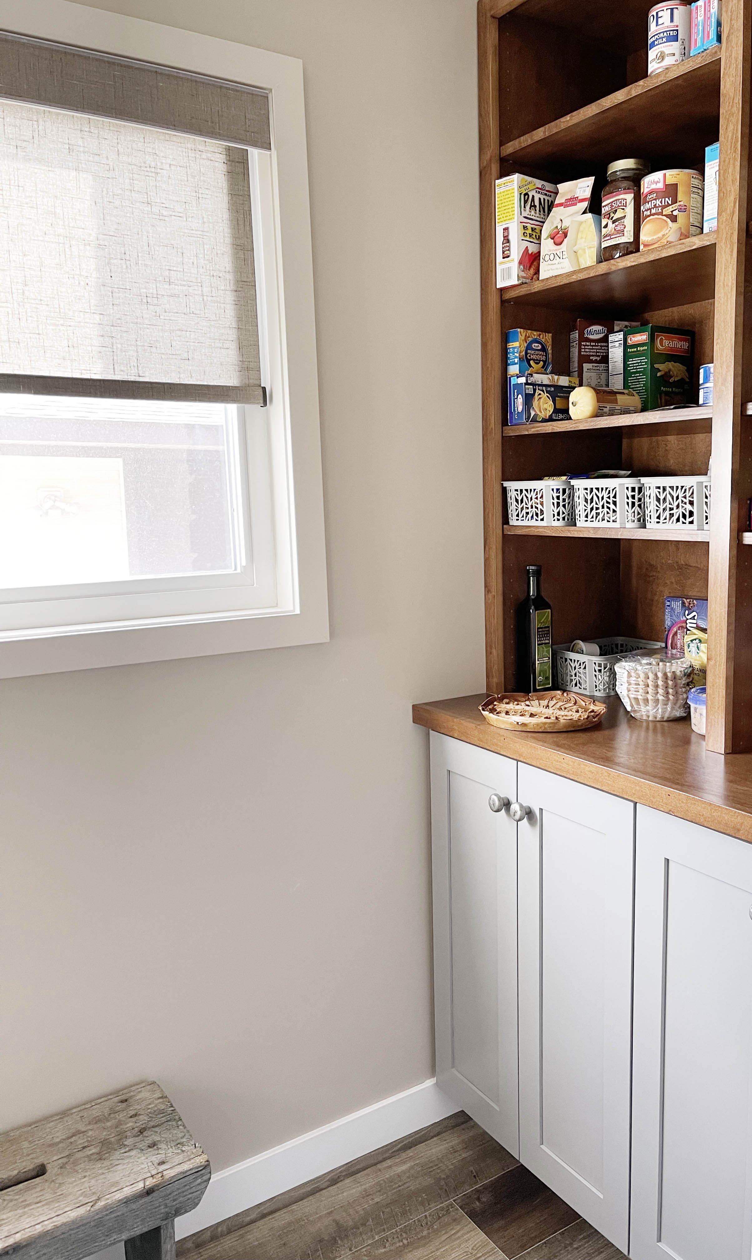 Shelf filled with various food items beside a window with a beige shade