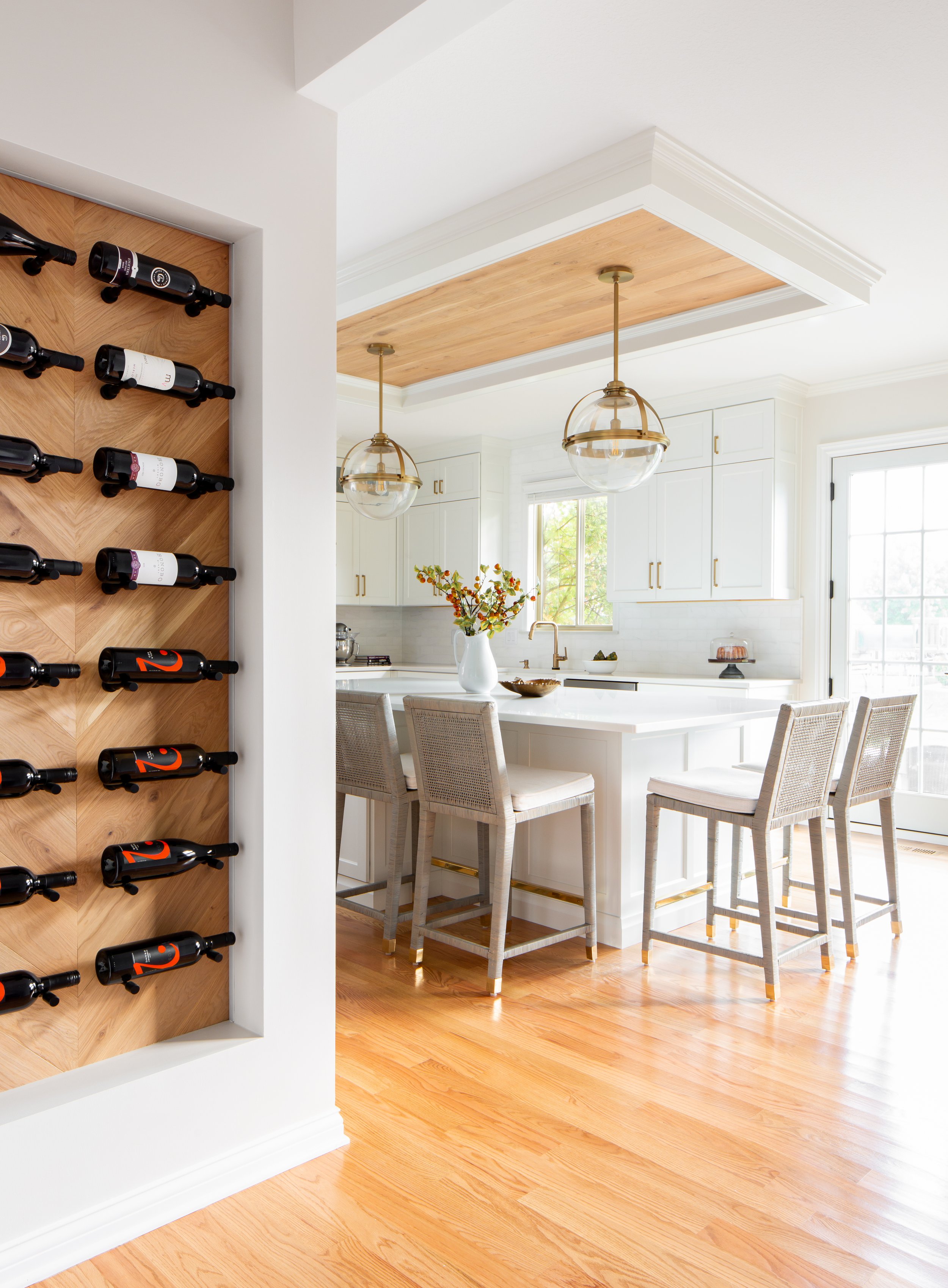 Modern kitchen and dining area with white cabinets, pendant lights, and a wine rack on a wooden wall.