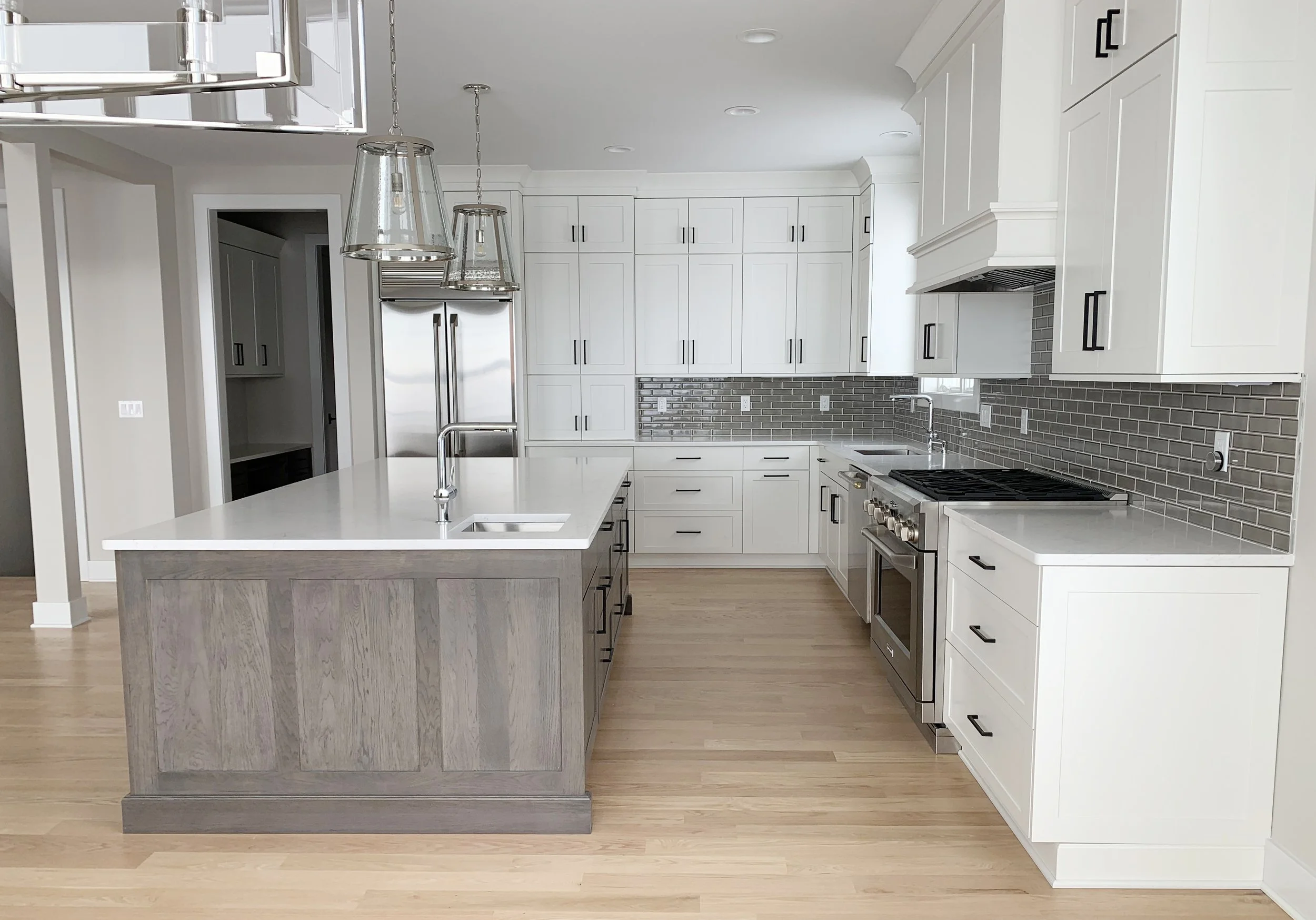 Modern kitchen with white cabinets, gray brick backsplash, stainless steel appliances, and a large island with a white countertop.
