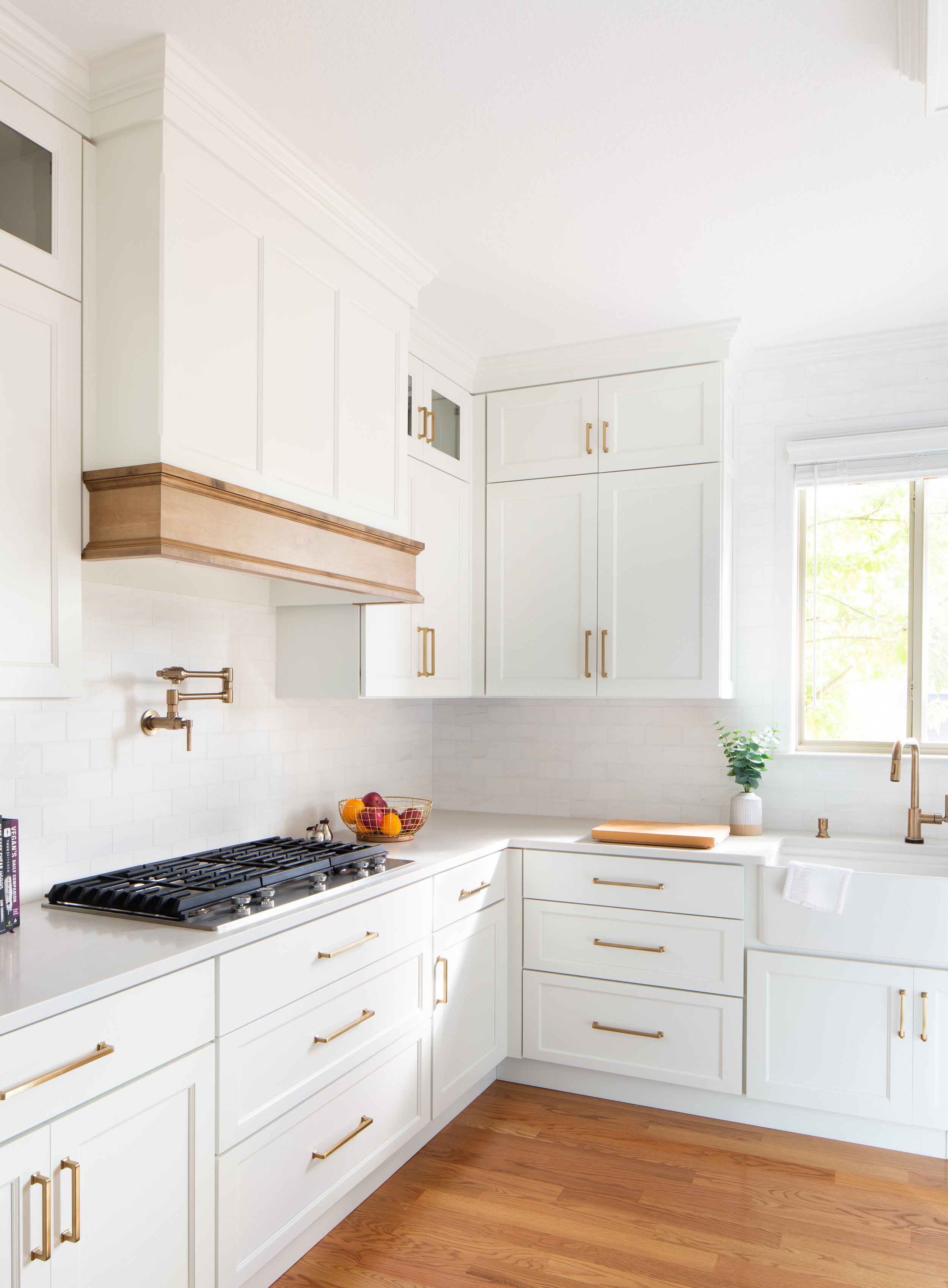 Bright white kitchen with gold hardware, wooden accents, fruit bowl, and a window with natural light.