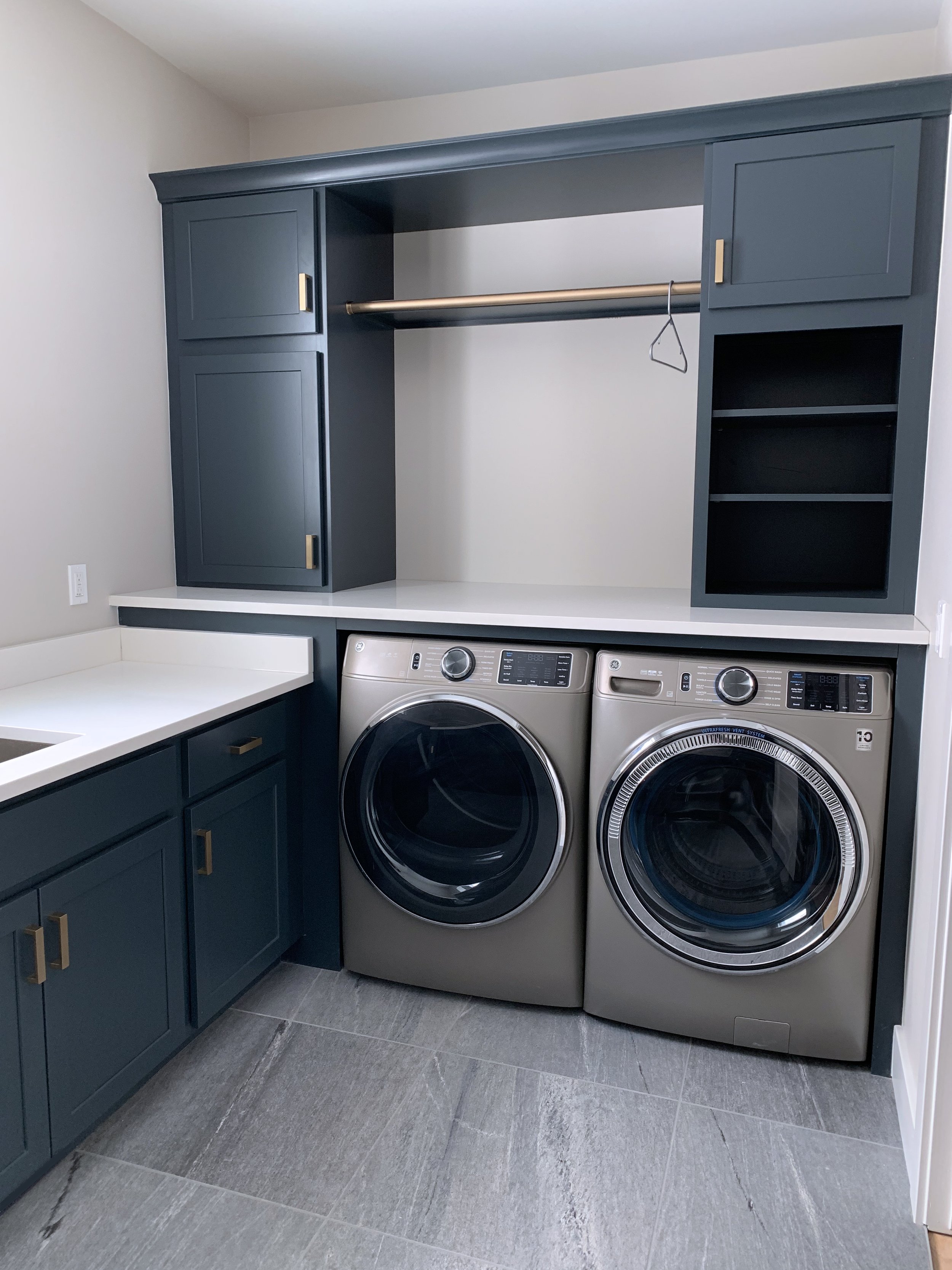 Laundry room with dark teal cabinets, white countertop, and a front-loading washer and dryer side by side.