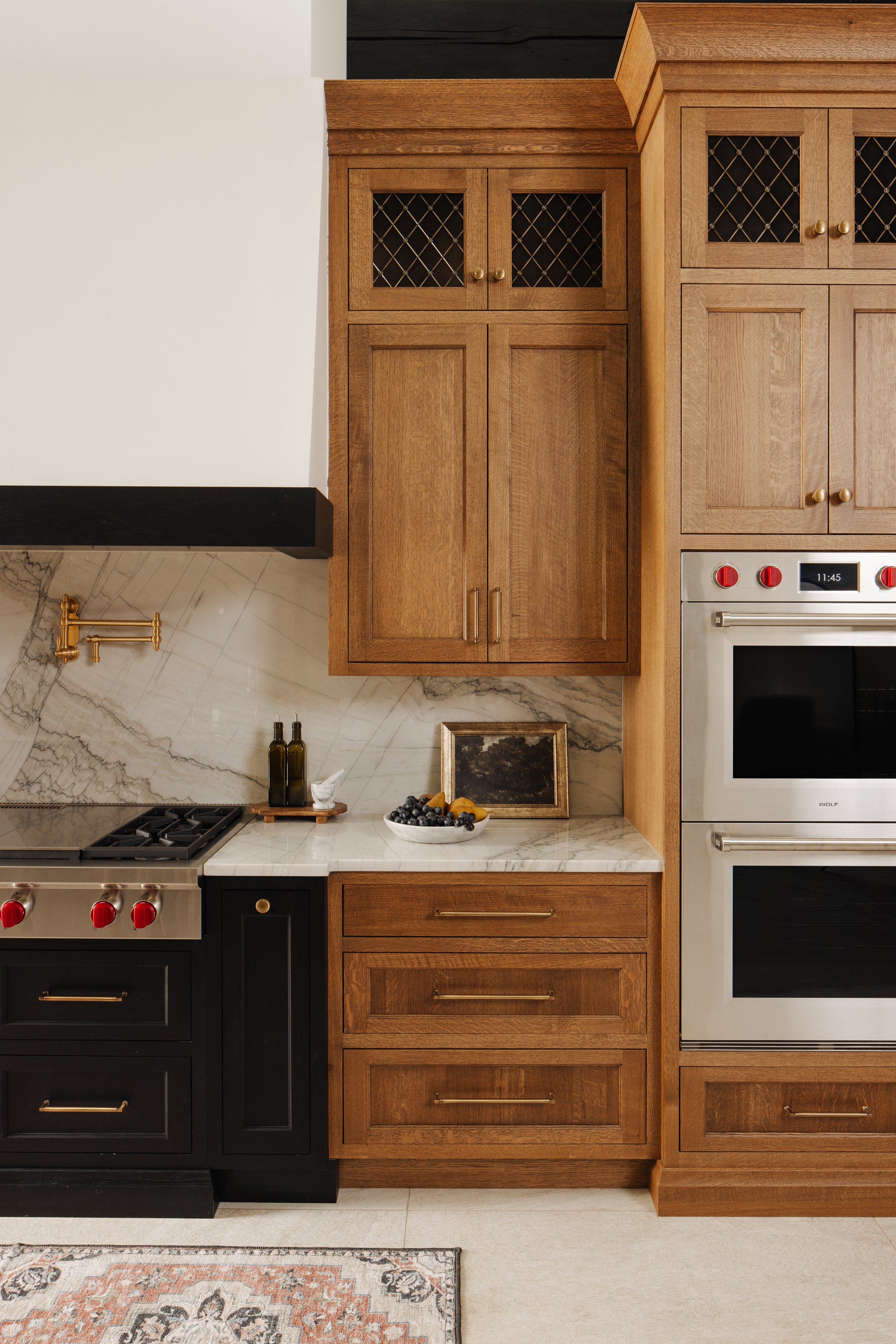 Kitchen with wooden cabinets, marble backsplash, black and stainless steel appliances, and decorative items like a bowl of fruit and bottles on the counter.