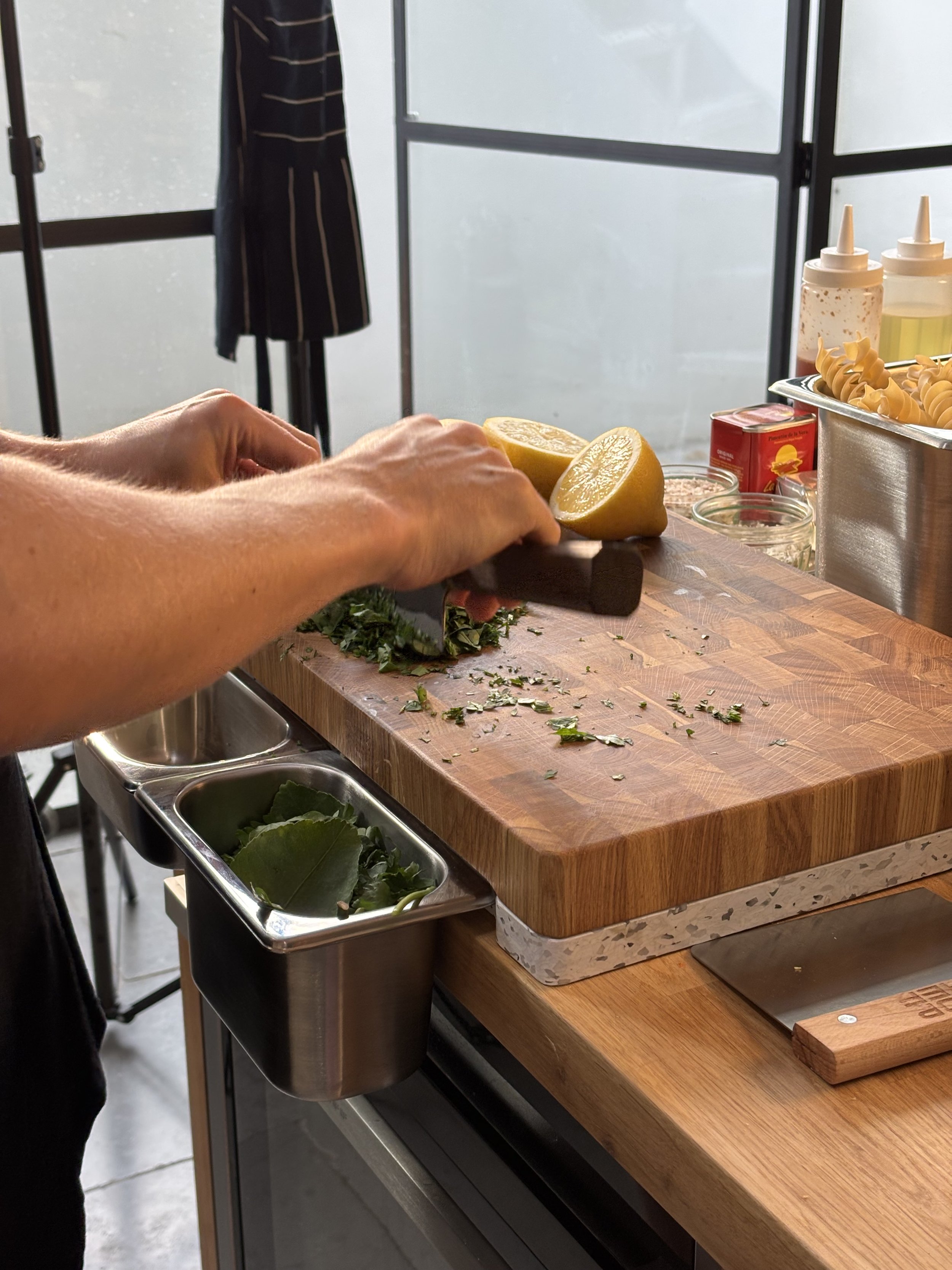 Person chopping herbs and lemons on a wooden cutting board in a kitchen.