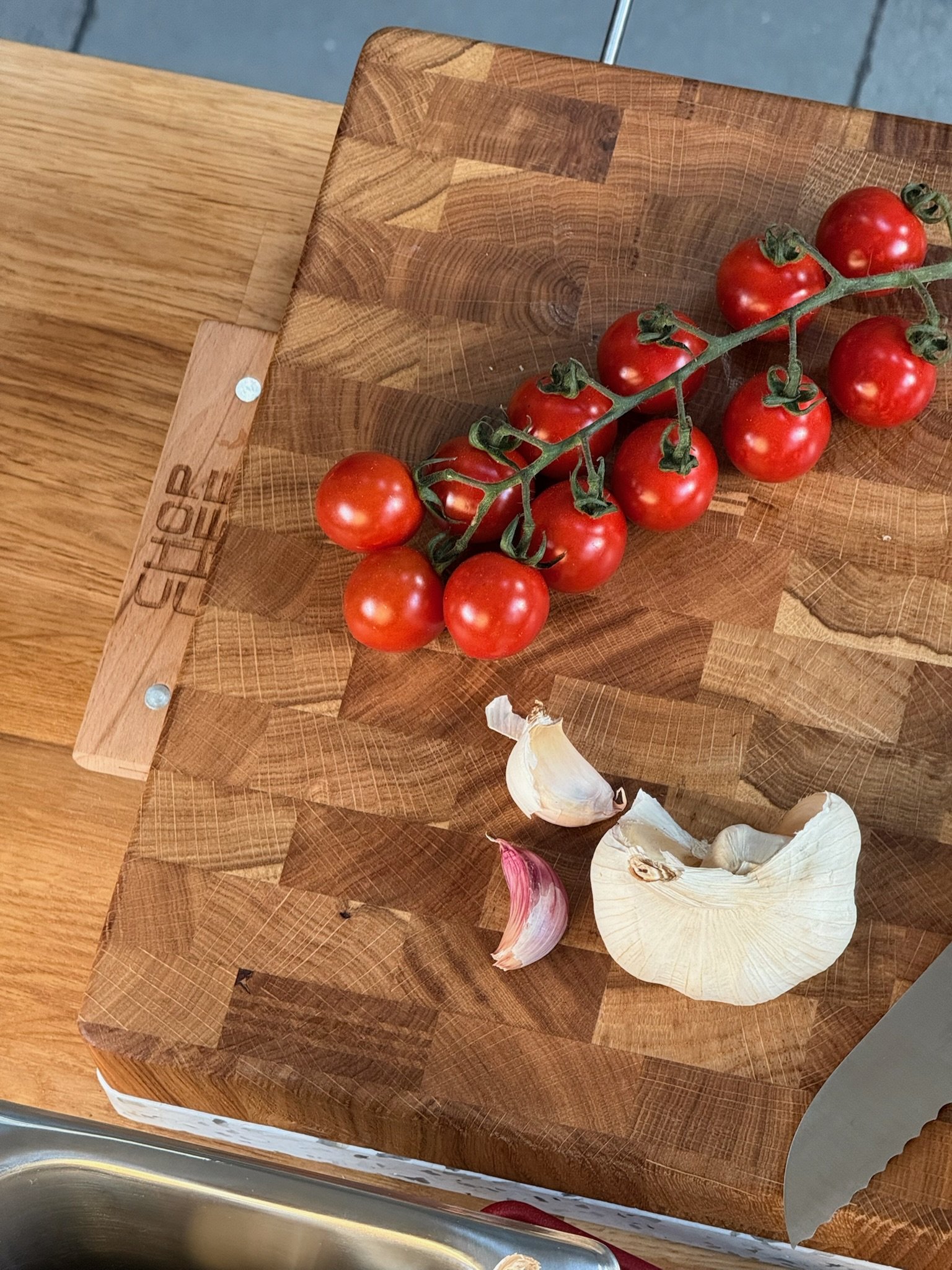 A wooden cutting board with cherry tomatoes on the vine and garlic cloves.