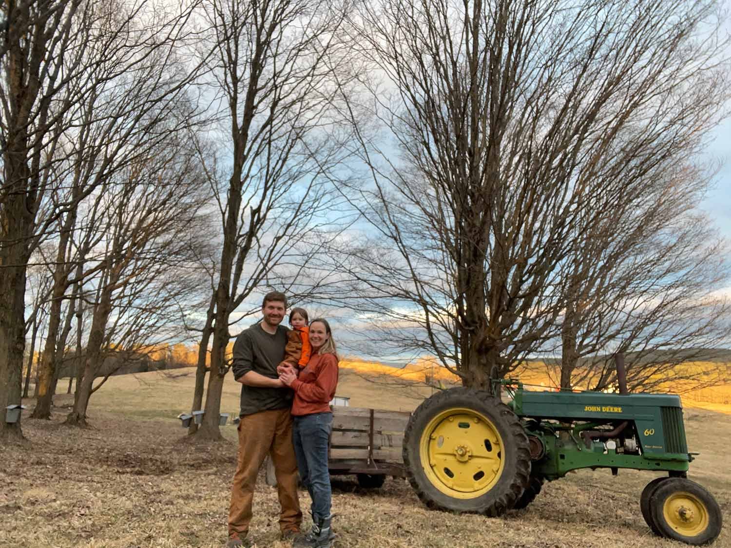 Seth and Sandy Chidester holding child in front of tractor and trees