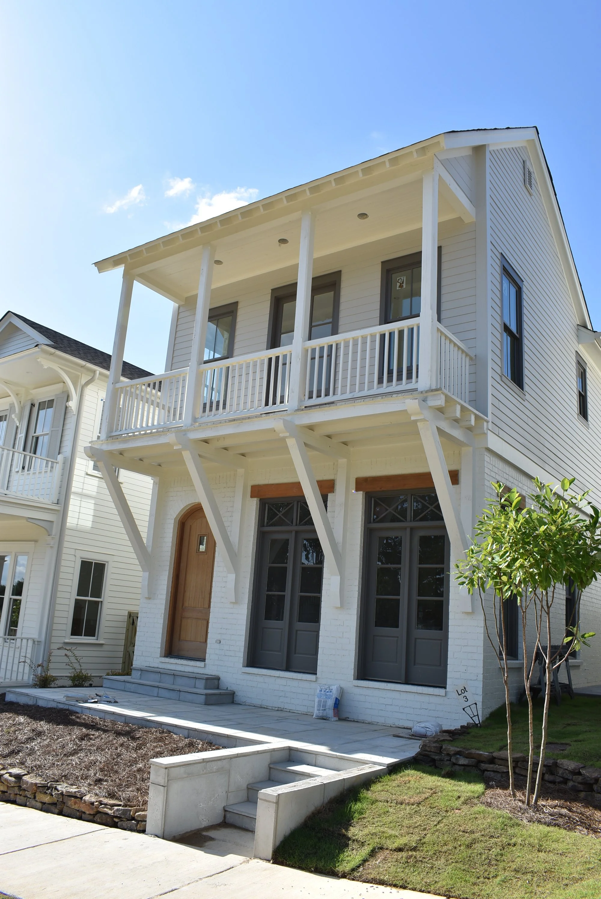 A two-story white house with a small front porch and balcony, gray door, and white railings, under a blue sky with some clouds.