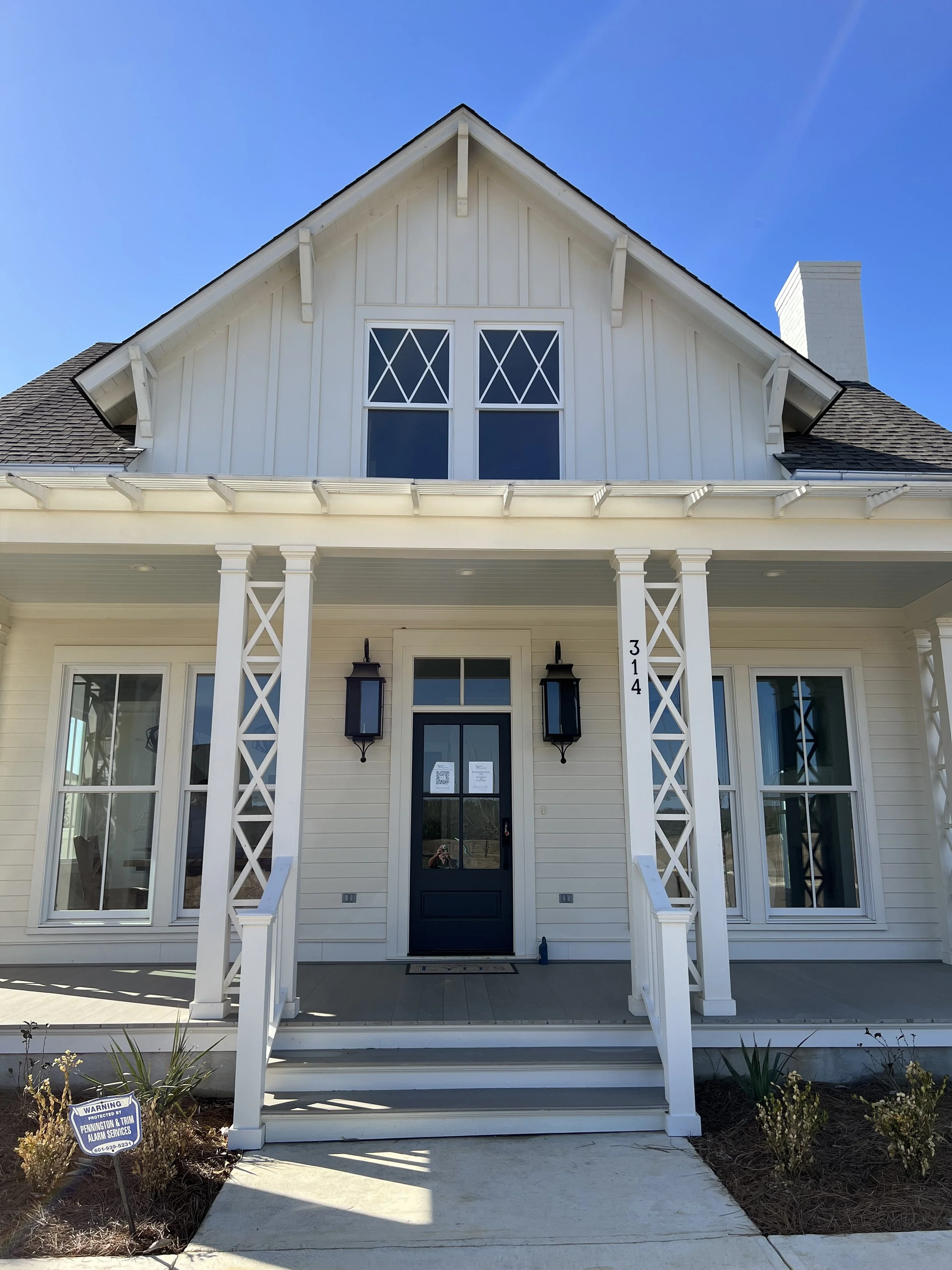 Front view of a two-story white house with a porch, black door, and decorative porch columns, numbered 314, under a blue sky.