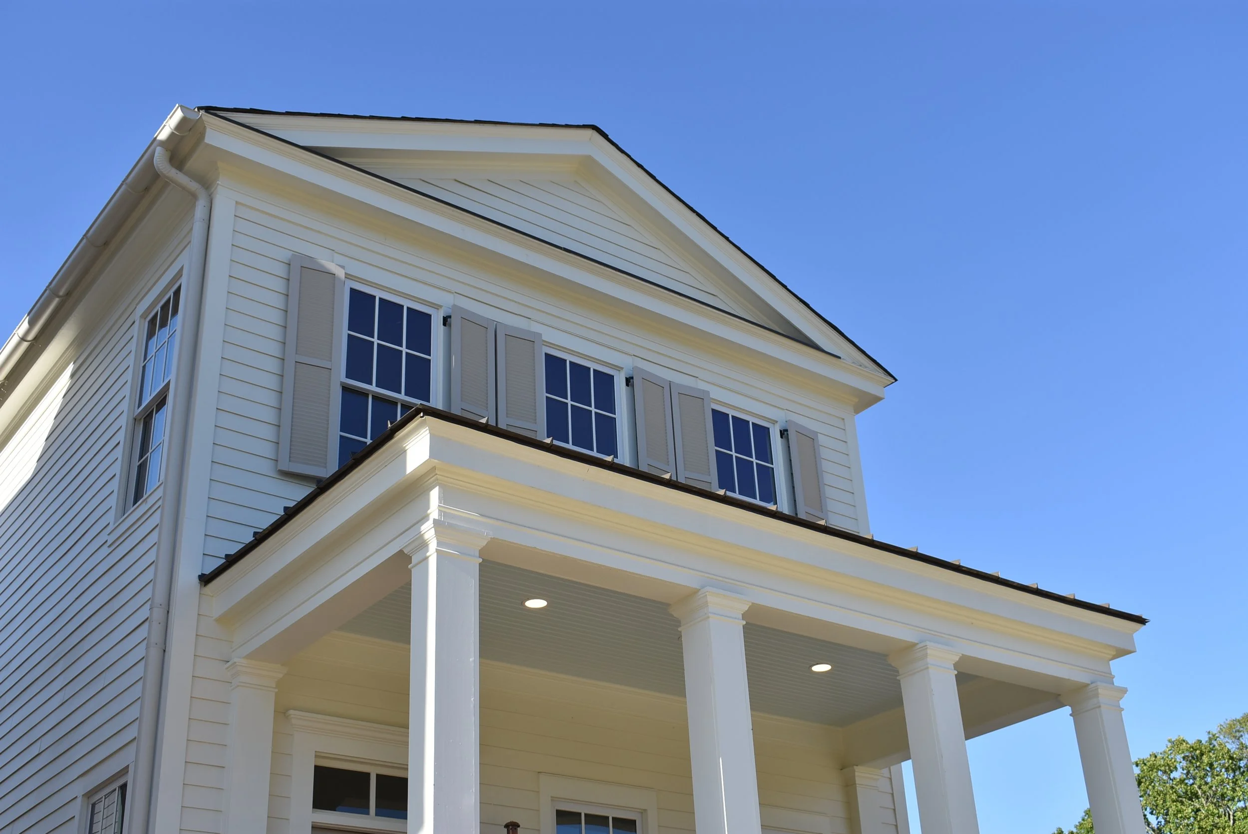 A white two-story house with a porch, columns, and multiple windows under a clear blue sky.