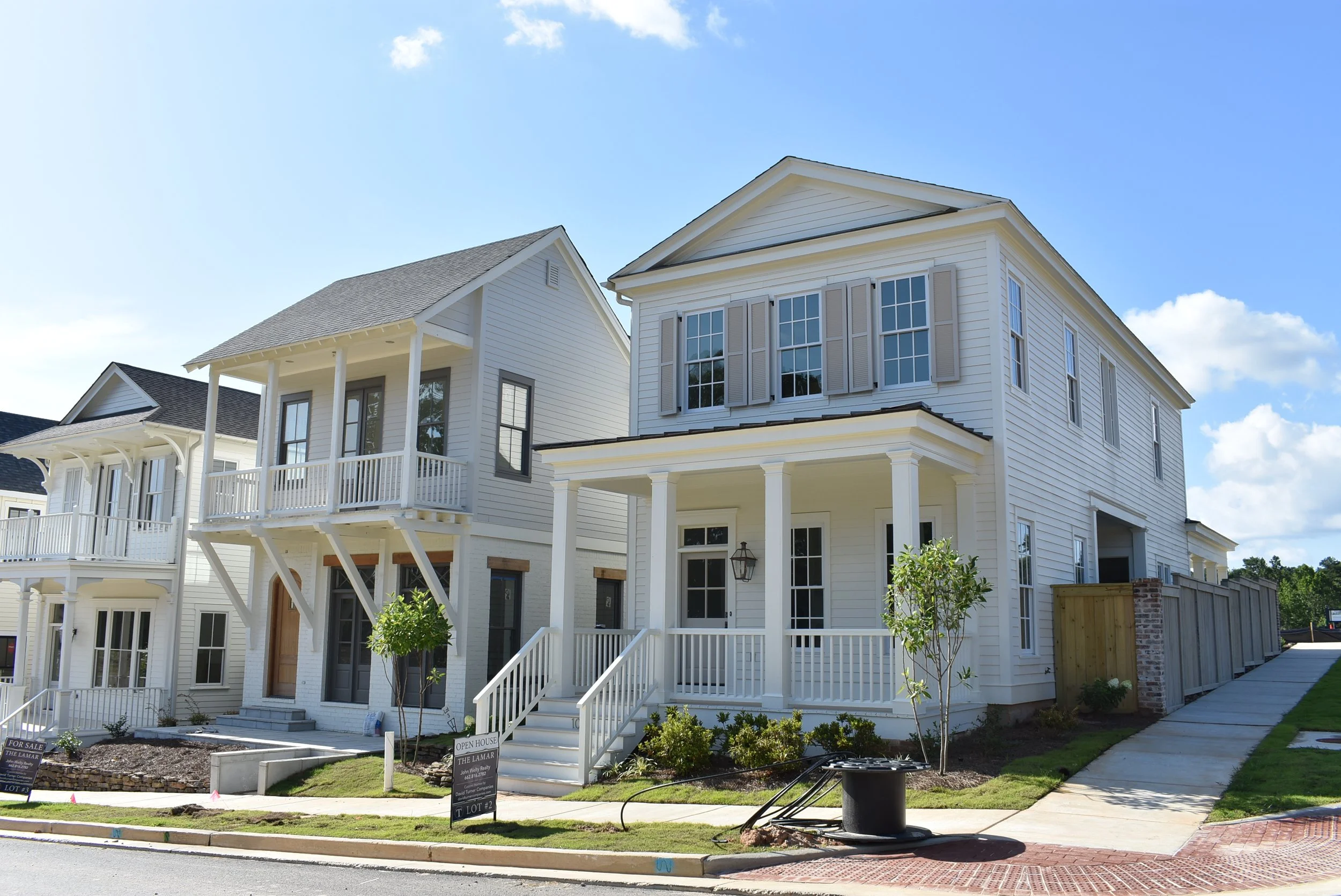 New white, multi-story homes with porches and small trees in front, under a blue sky with some clouds.