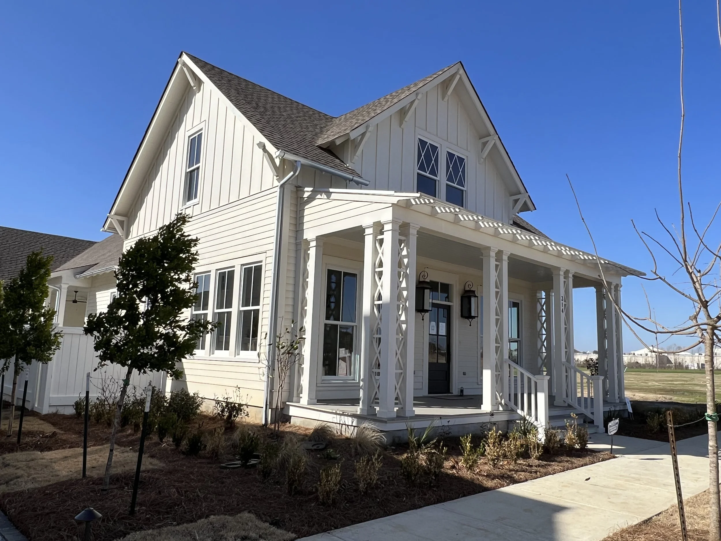 White two-story house with a front porch, black door, and decorative trim, under a clear blue sky.