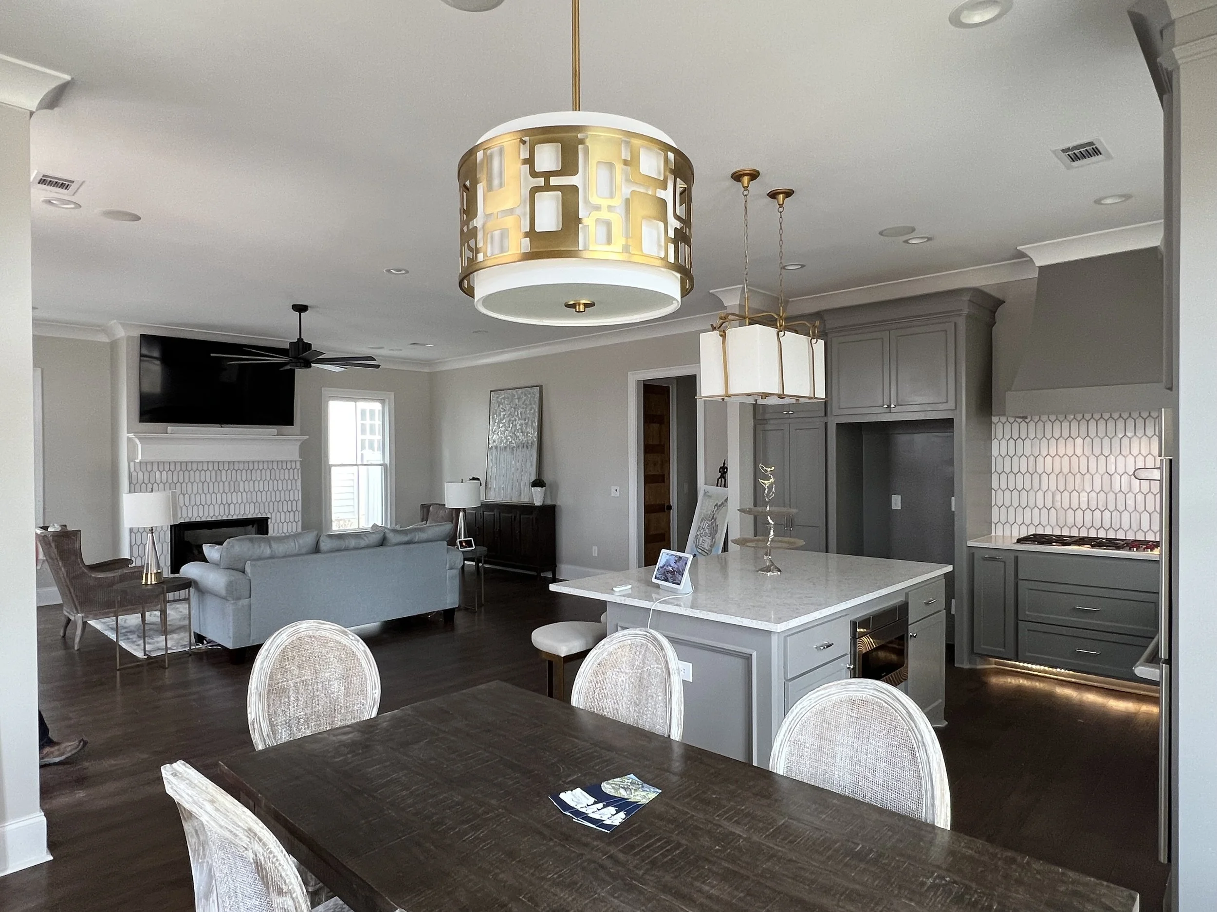 Open-concept living and kitchen area with modern decor, hardwood floors, a dining table, light fixtures, a sofa, TV, fireplace, and a window in the background.