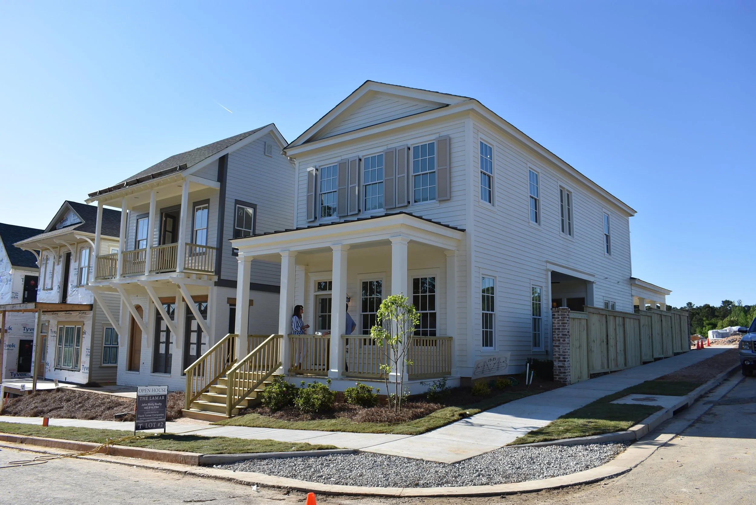 Newly built multi-story house with white vinyl siding, front porch with columns, and several windows, under a clear blue sky.