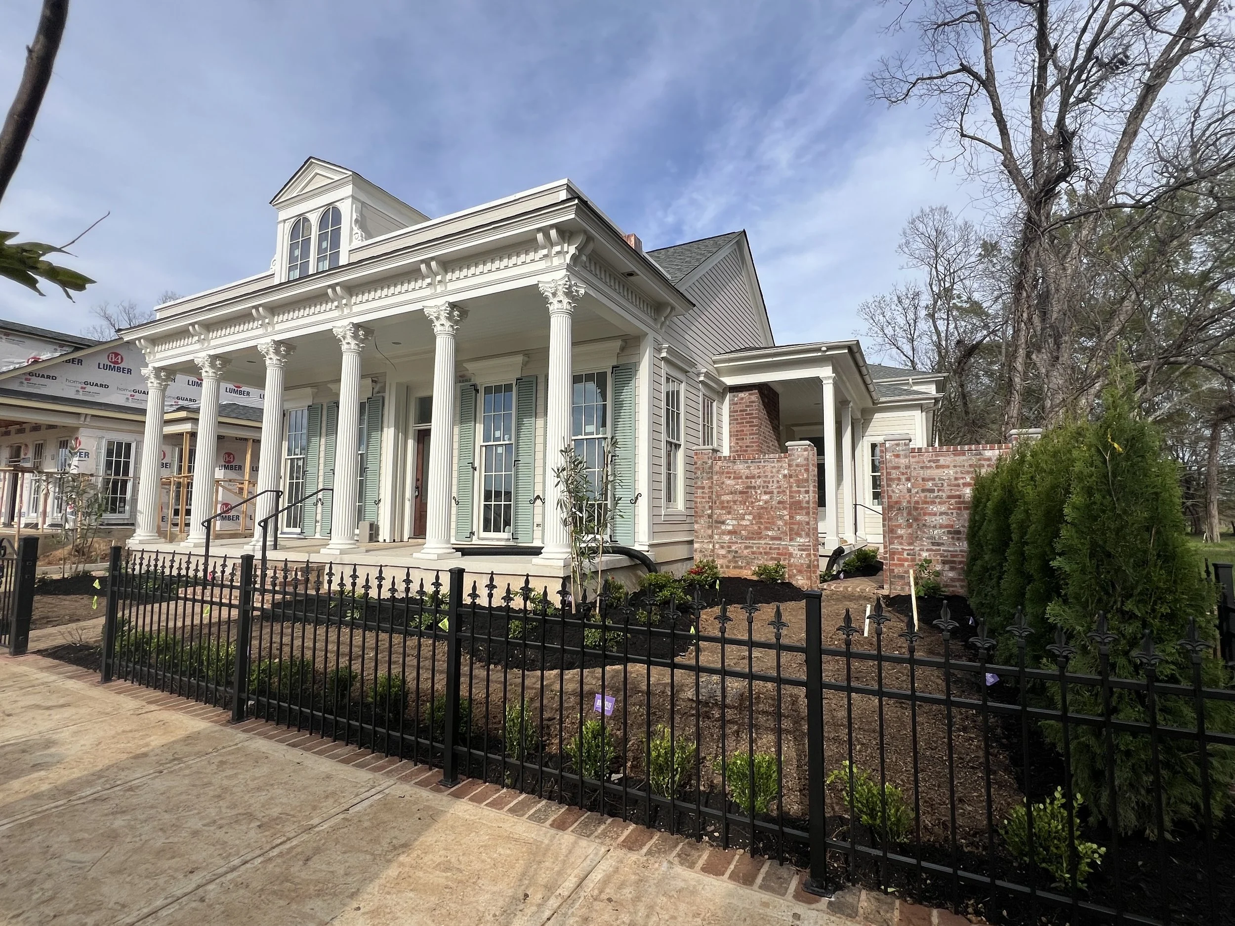 Newly constructed white house with classical columns, front porch, and landscaping, with a cloudy sky above.
