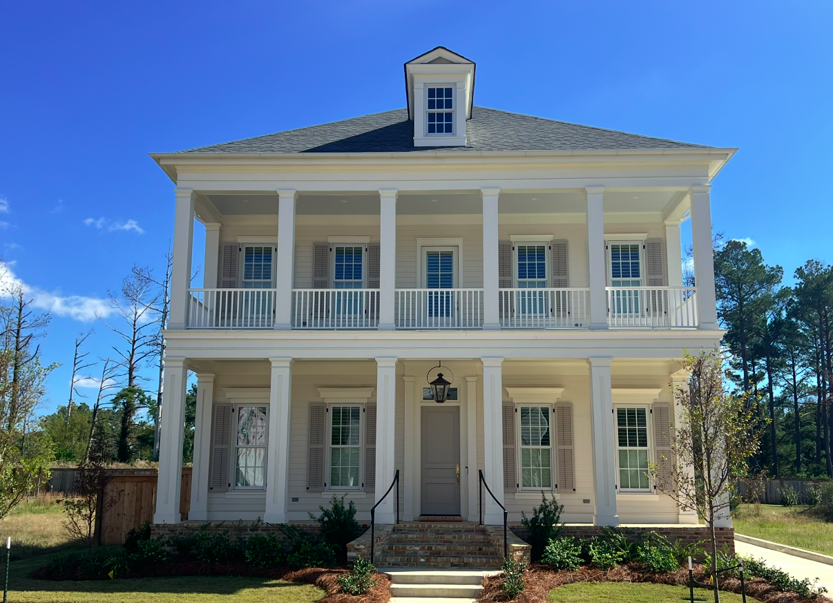 White three-story house with front porch, balcony, and dormer window under a blue sky.
