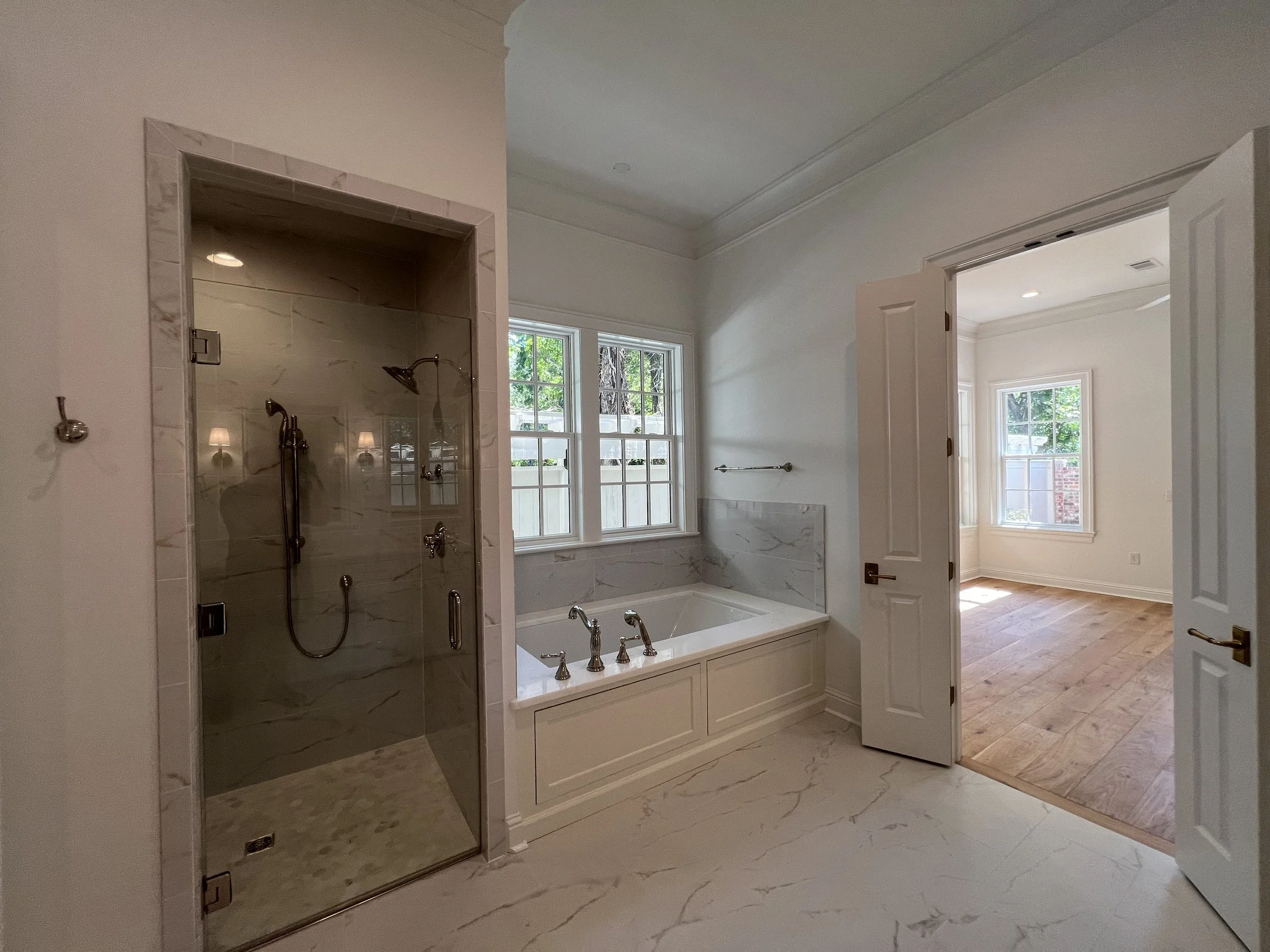 Bathroom with walk-in shower, bathtub, and hardwood floor adjacent to a room with large windows.