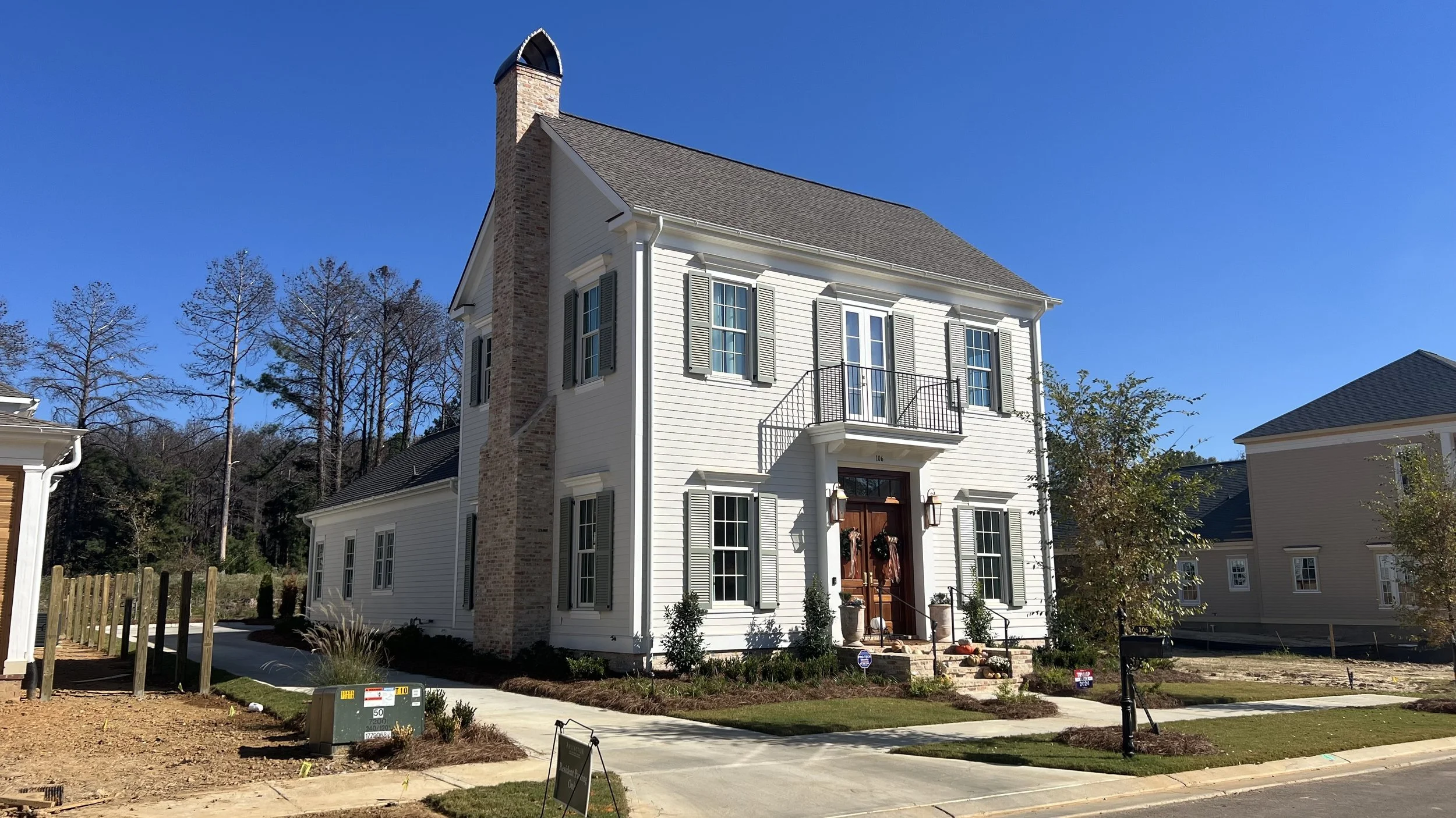 White two-story house with gray shutters, brick chimney, front porch and small landscaped yard