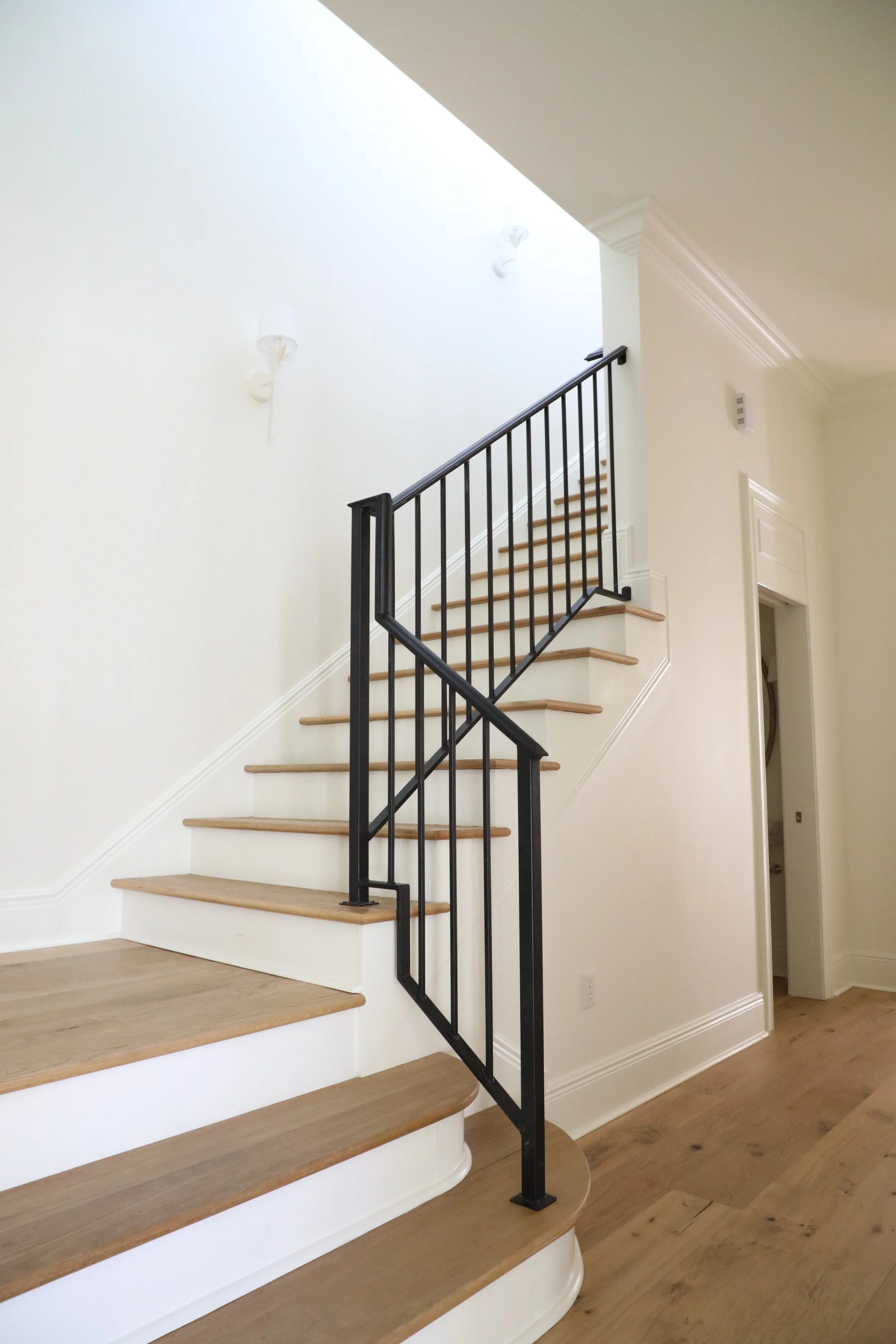 Interior view of a staircase with wooden steps, a black metal railing, white walls, and a ceiling with crown molding.