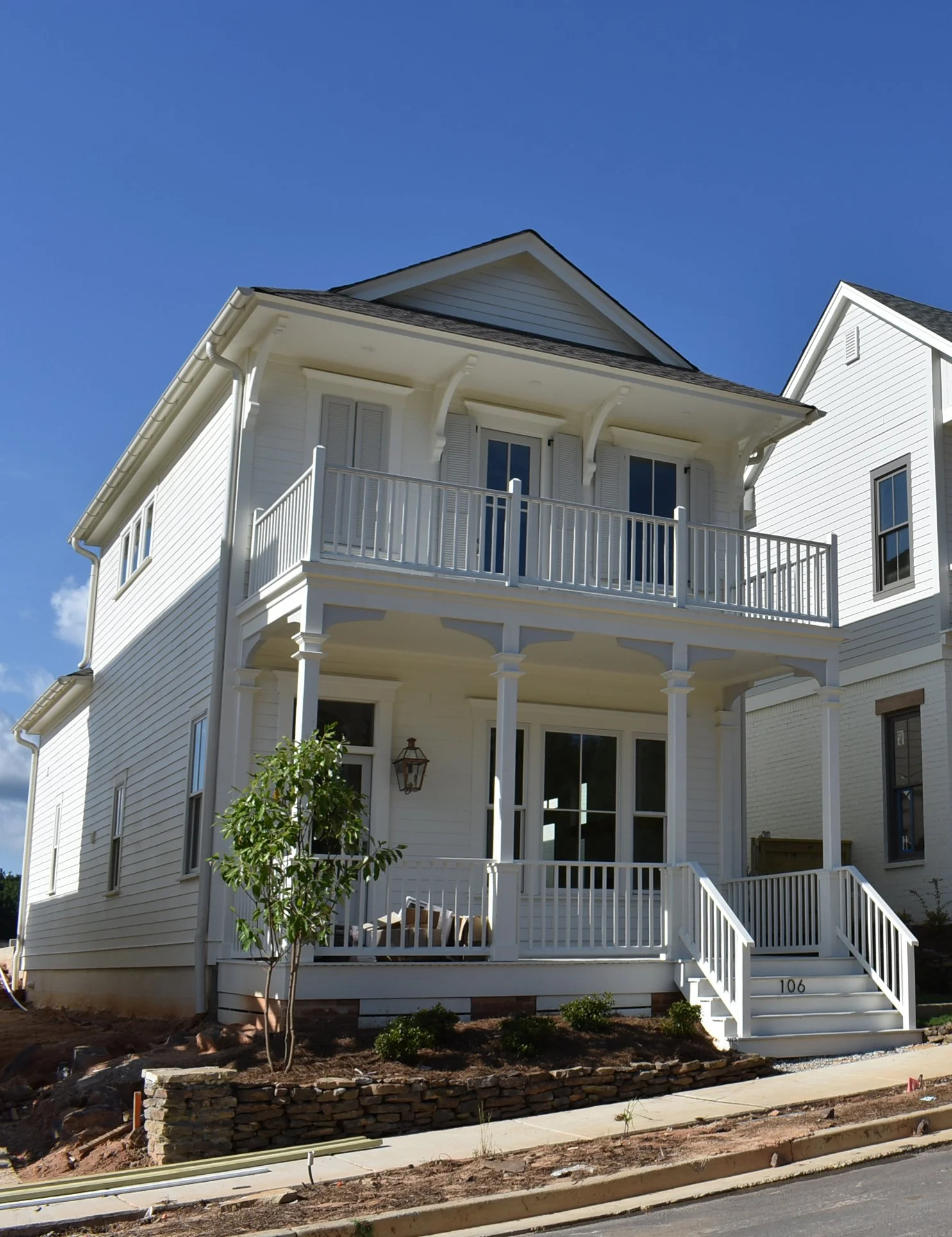 A three-story white house with a front porch, second-story balcony, and black roof, under a clear blue sky.