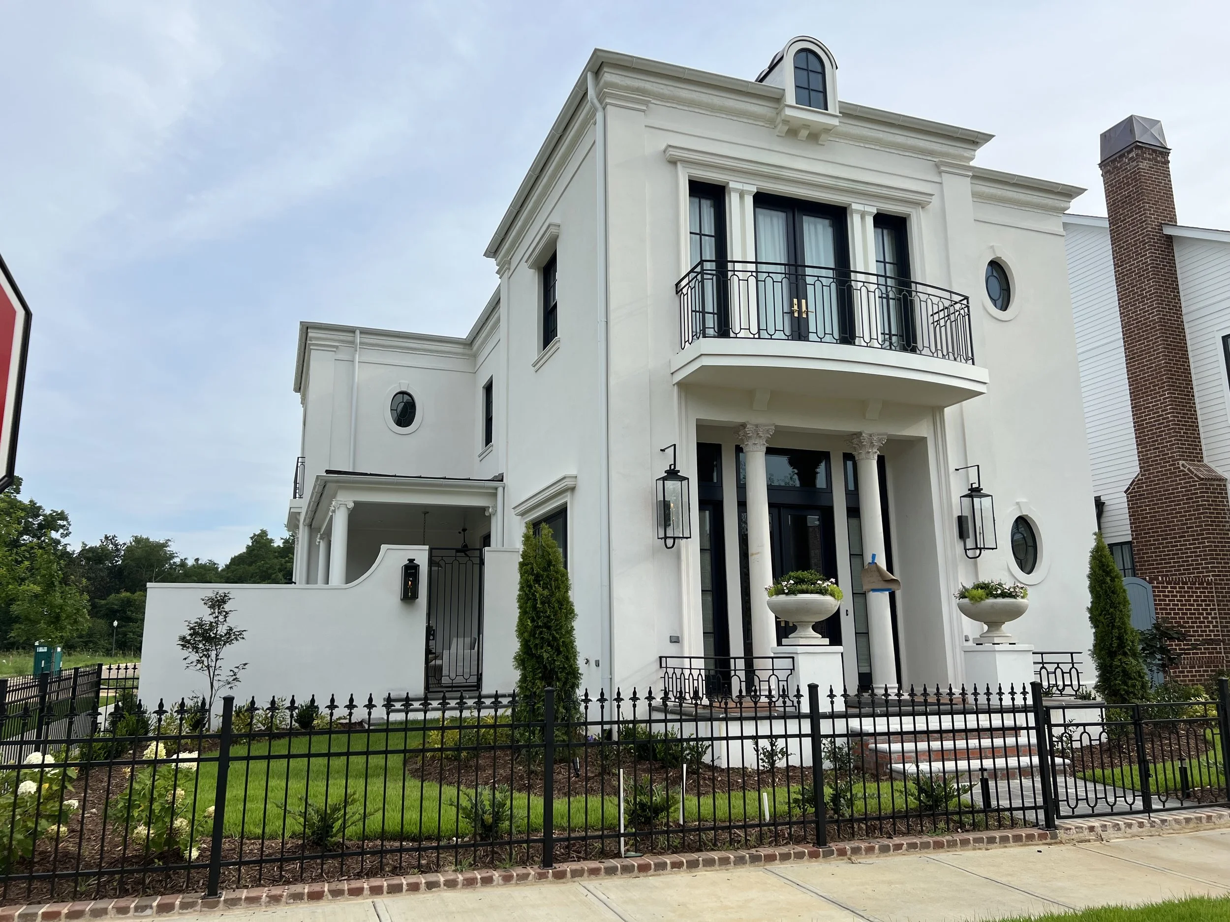 White modern house with black door, columns, iron railings, and lush landscaping