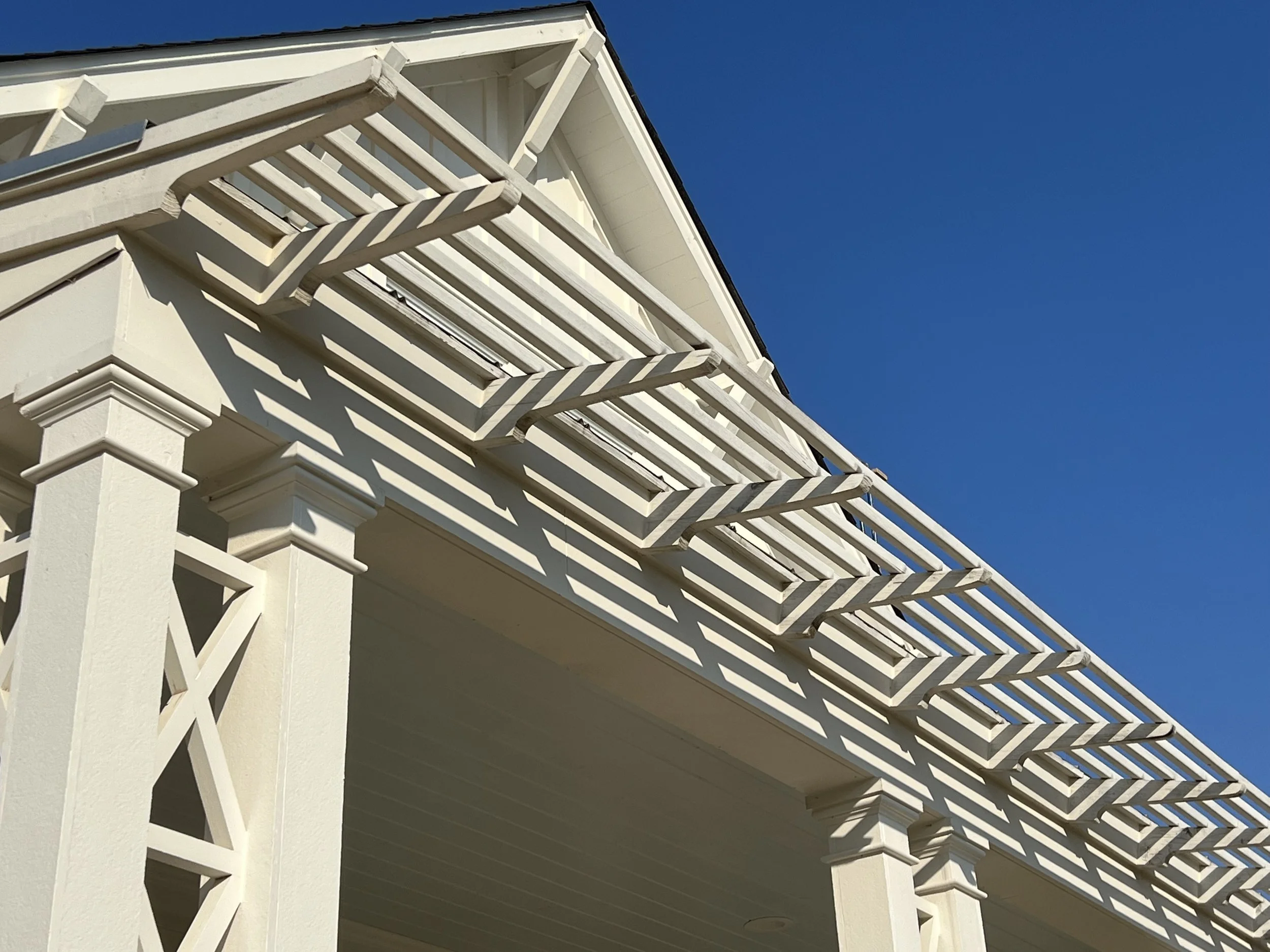 White wooden pergola with slatted roof on a house against a clear blue sky.