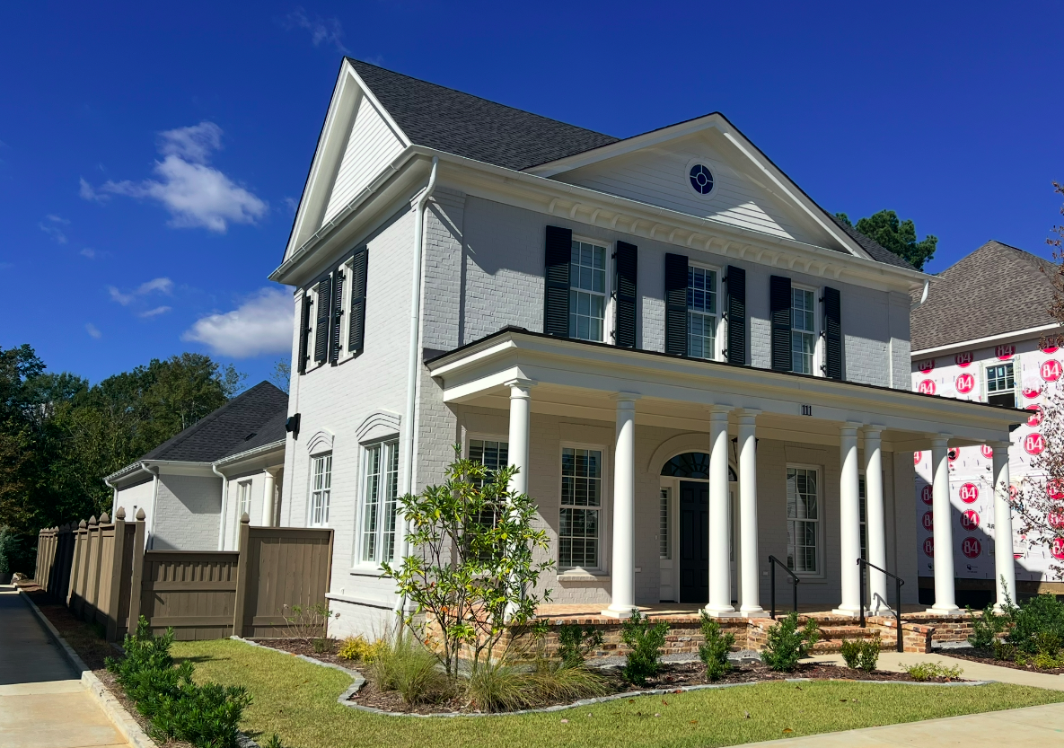 New white two-story house with black shutters, columns on the porch, and brick steps, under a clear blue sky.