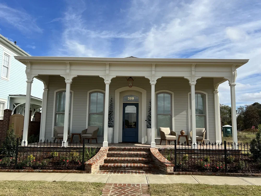 Front view of a vintage-style house with porch, brick stairs, outdoor seating, and a garden.