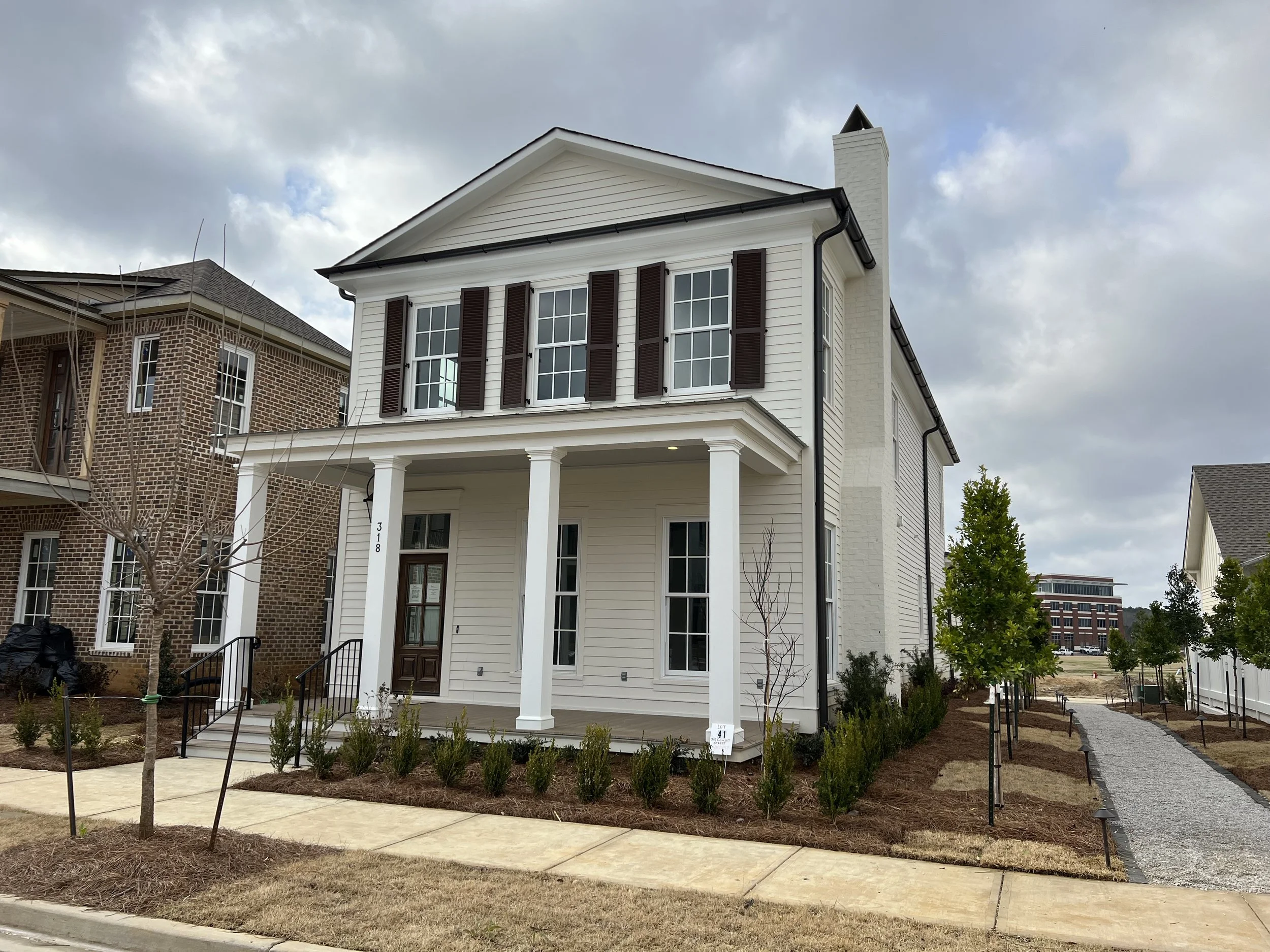 New white two-story house with black shutters and front porch, under cloudy sky, with landscaped yard and gravel walkway.